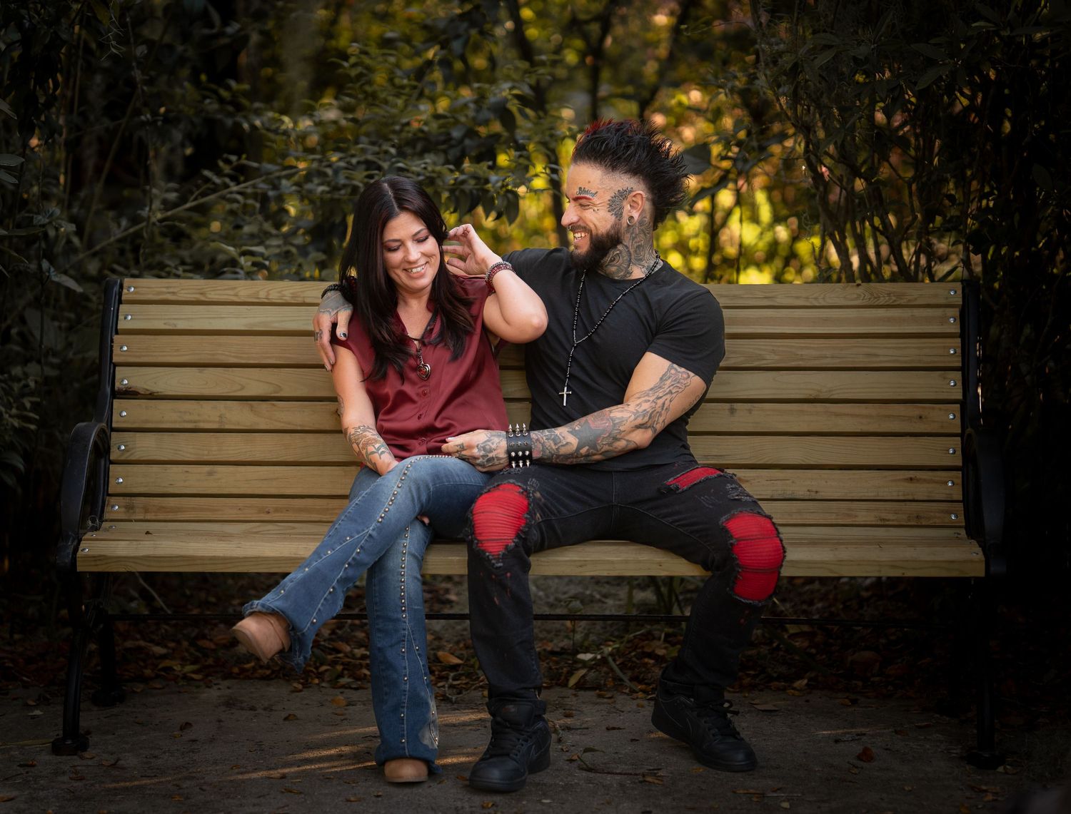 Tattooed couple sharing a playful moment on a wooden park bench outdoors.