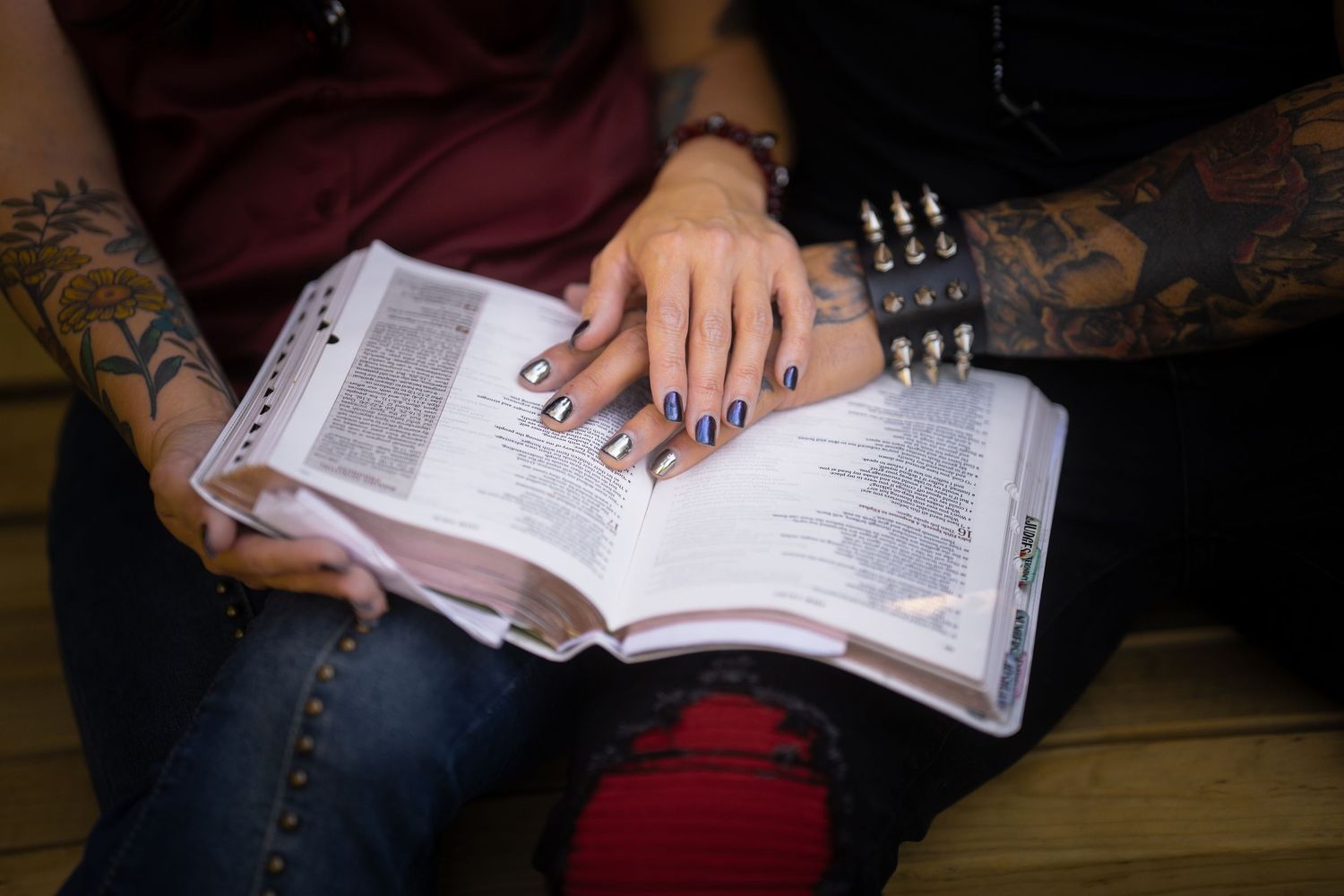 Tattooed couple reading a Bible together with hands resting on the open pages.