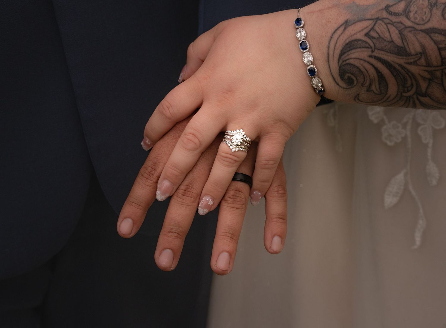 Close-up of couple's hands showing wedding rings, bracelet, and tattoo on wrist.