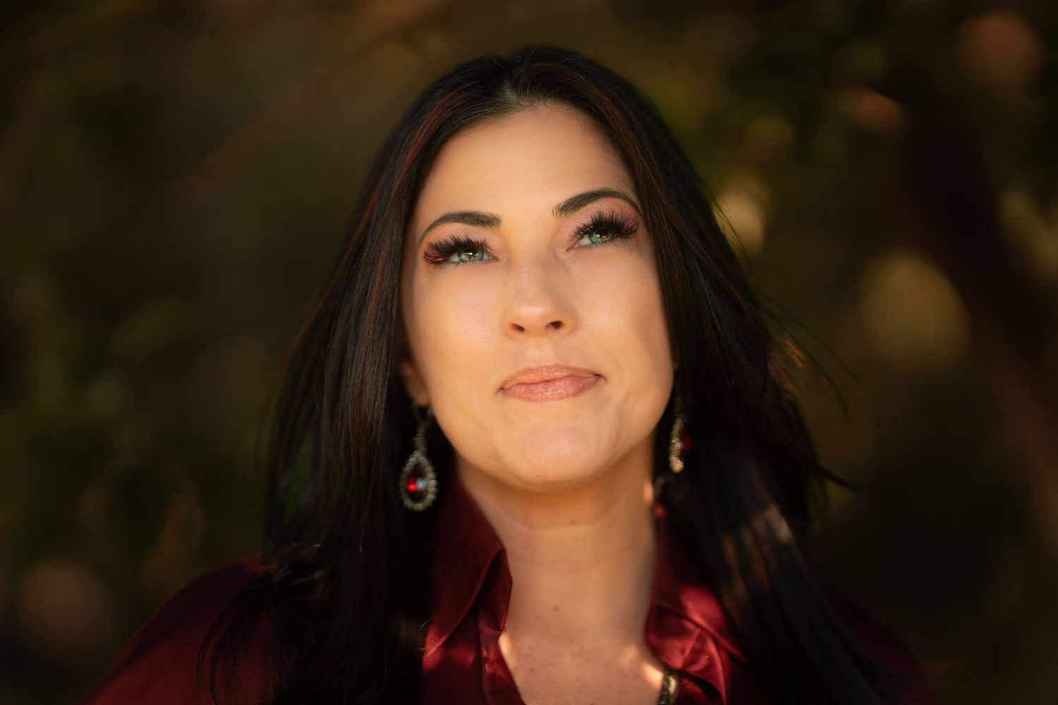 Beautiful dark-haired woman with turquoise earrings poses outdoors in warm autumn light.