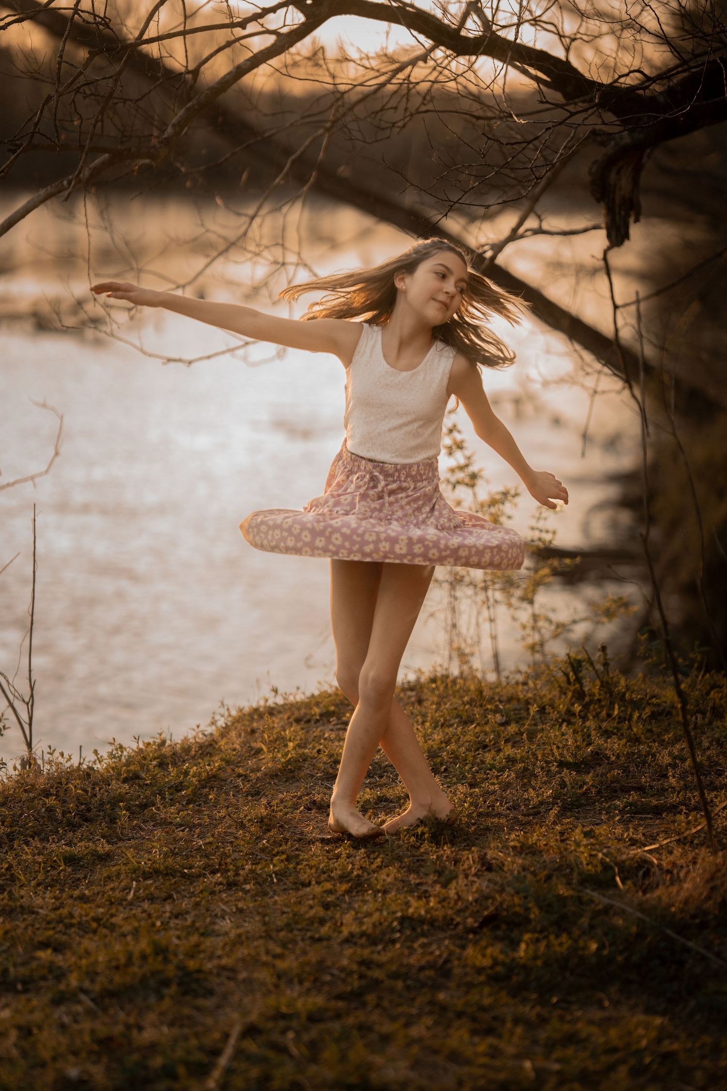 Carefree young girl twirls in pink skirt near river at golden hour sunset.