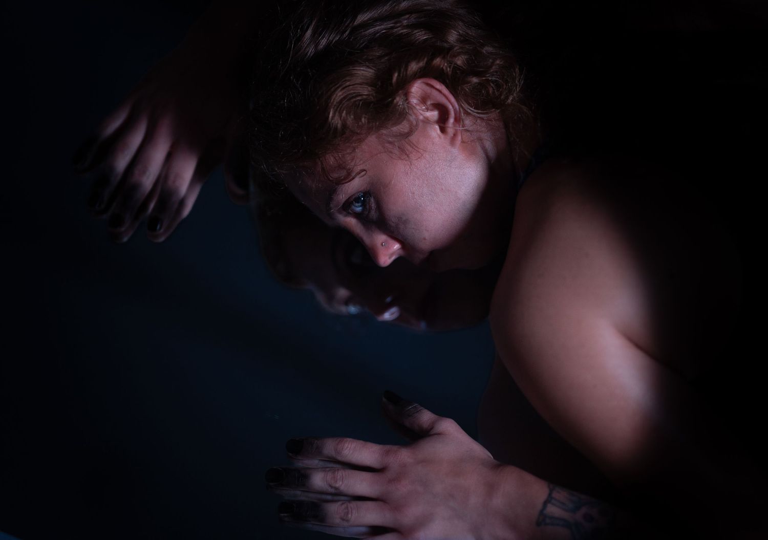 A person with curly hair rests their head down in dim blue light, hands visible in an emotional, moody portrait.