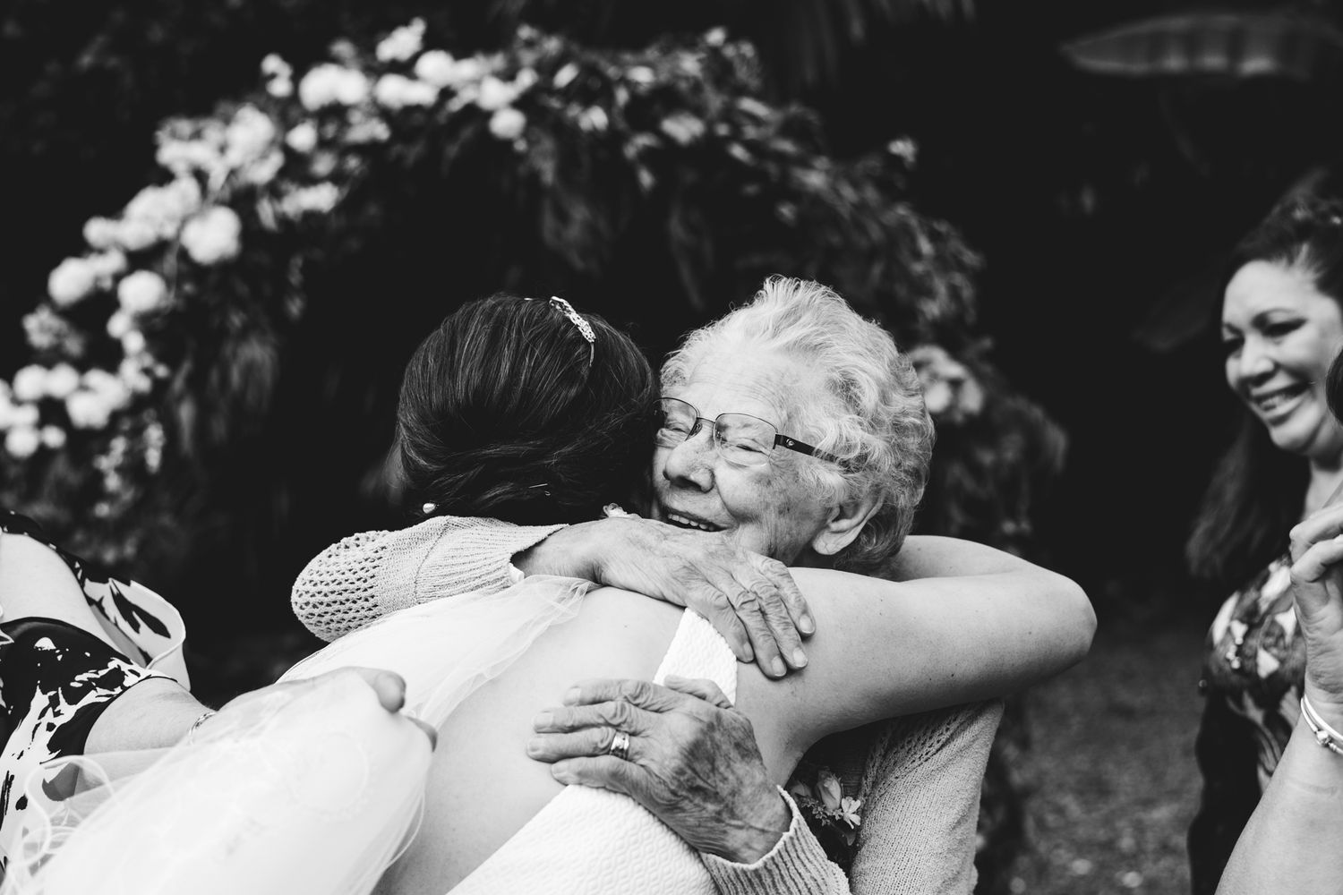 This Black and white image shows the strong embrace from a grandmother as she hugs her granddaughter in congratulations after she's married