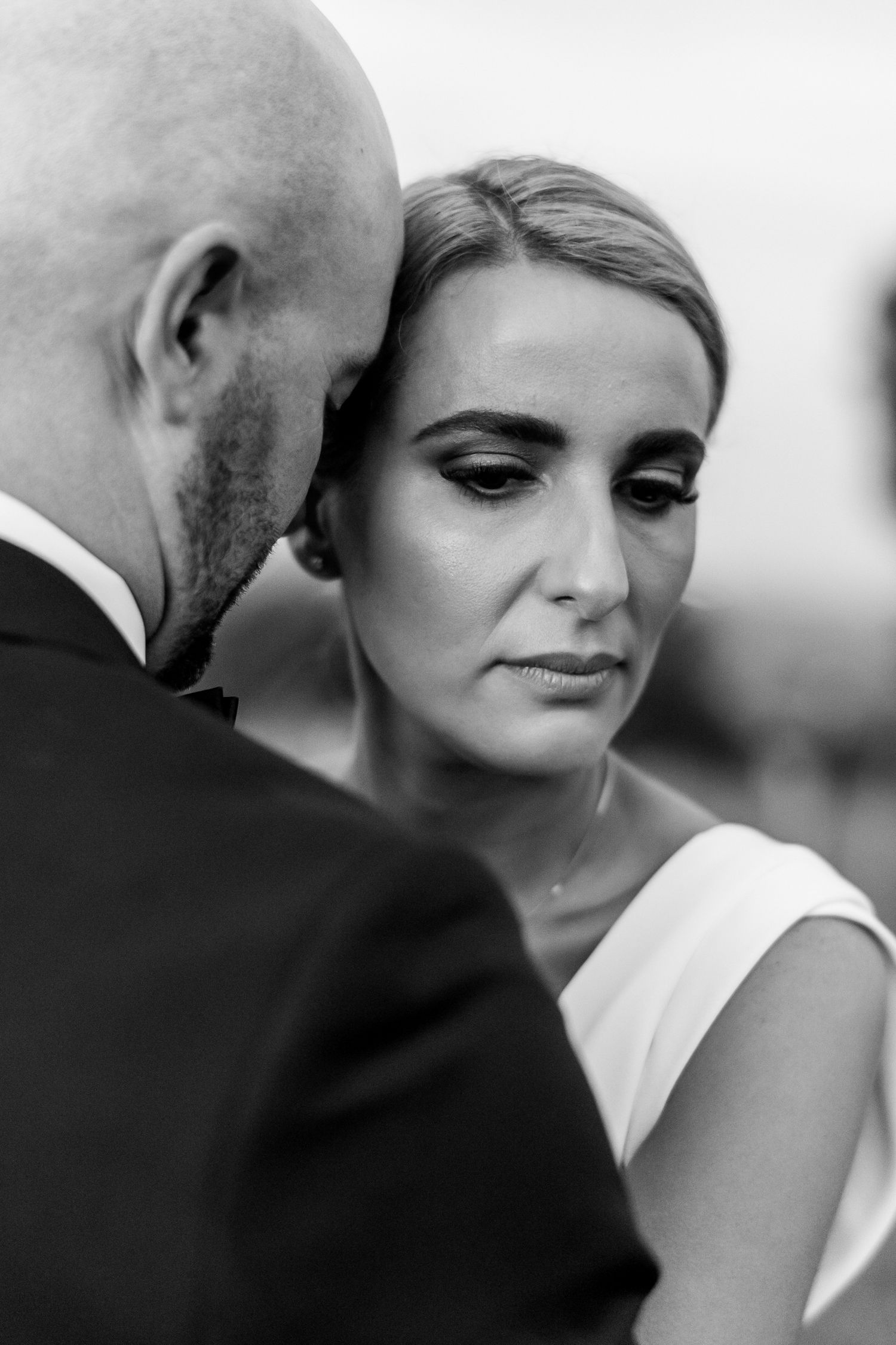 a close up of the brides face looking off to the side and downwards, the grooms head rests on her cheek