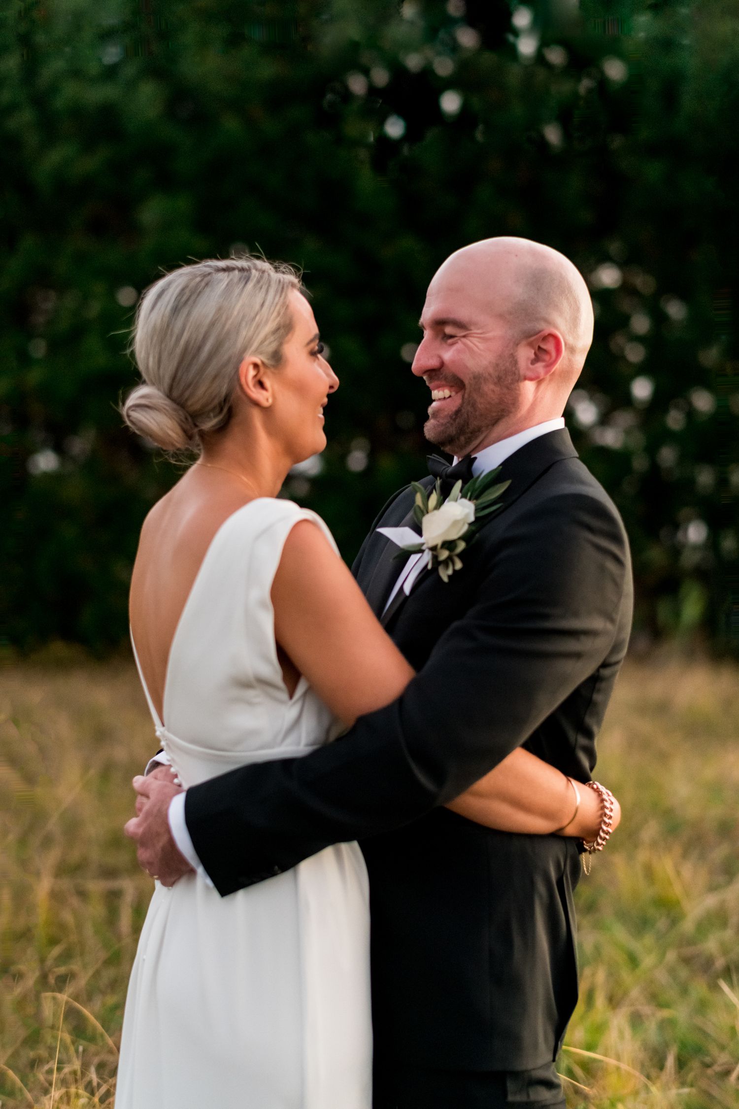 a bride and groom look at each other laughing arms wrapped around each other in the Mudbrick field