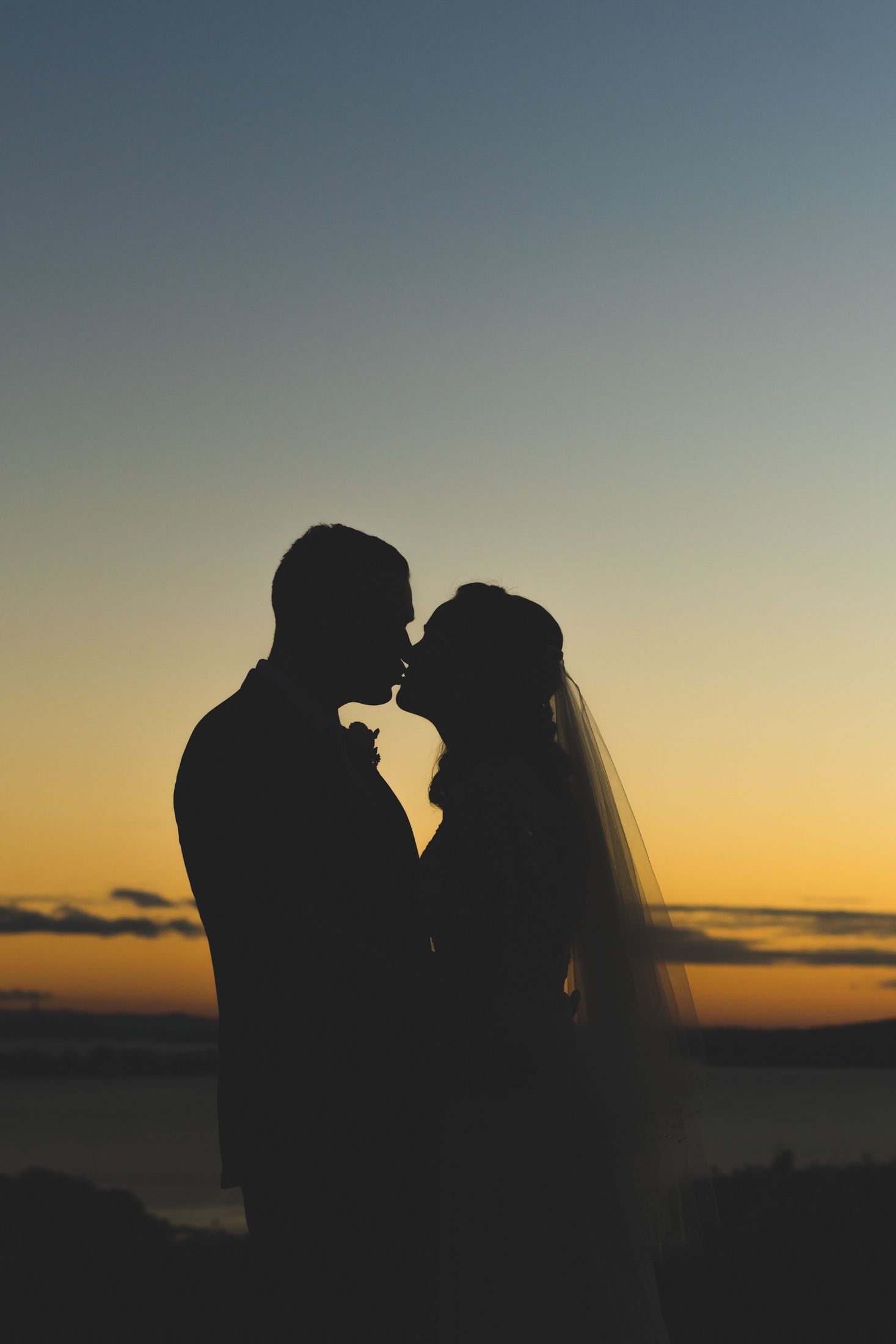 a silhouetted bride and groom portrait in front of a blue and yellow hued sunset