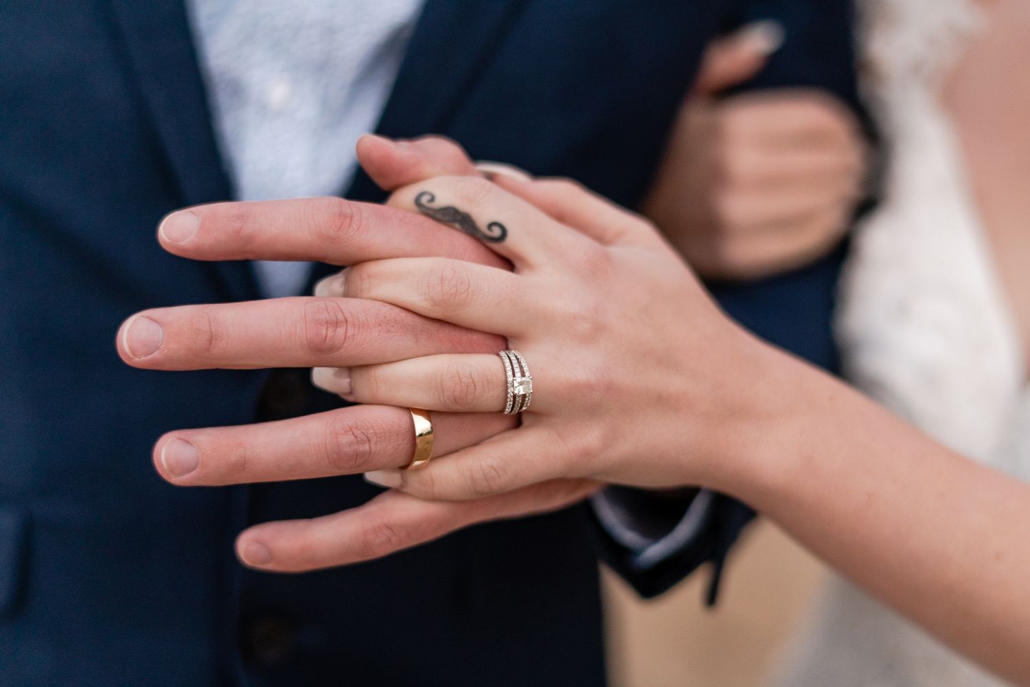 a close up of two hands entwined from a bride and groom showing off their wedding bands
