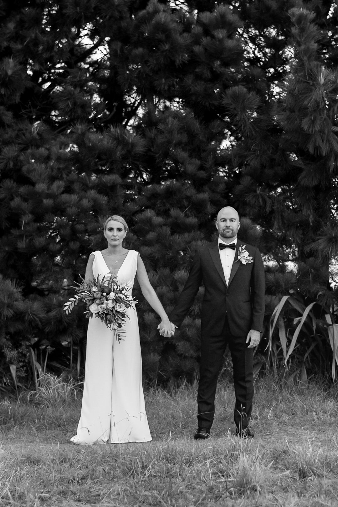 a black and white image of the bride and groom holding hands between them but both facing the camera straight on