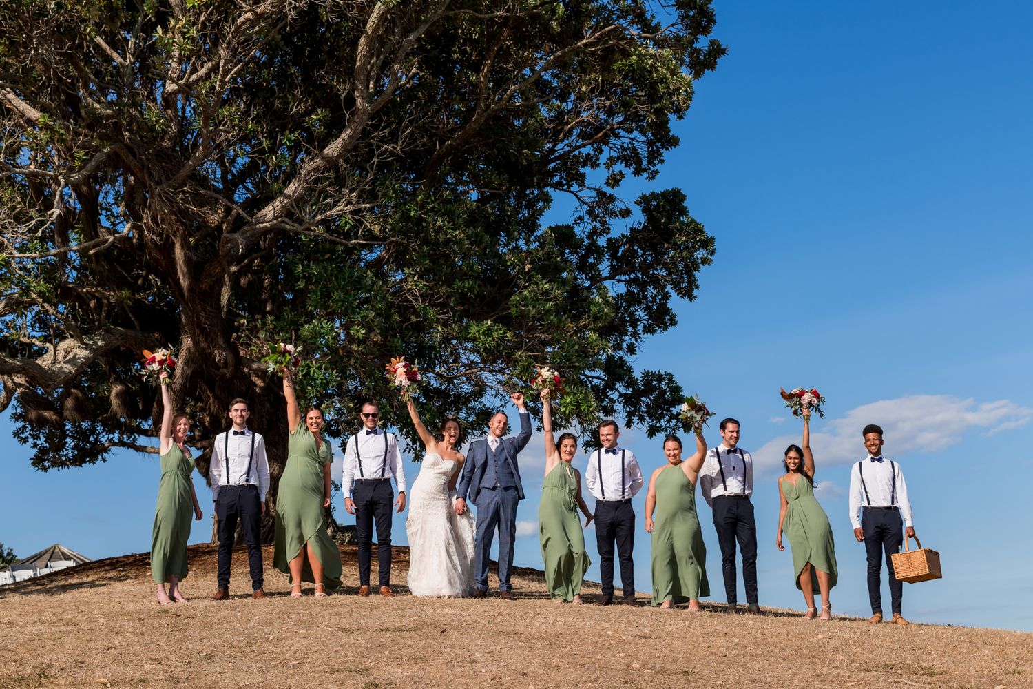 a wedding party stand on top of Goldie Hill with their hands in the air in celebration