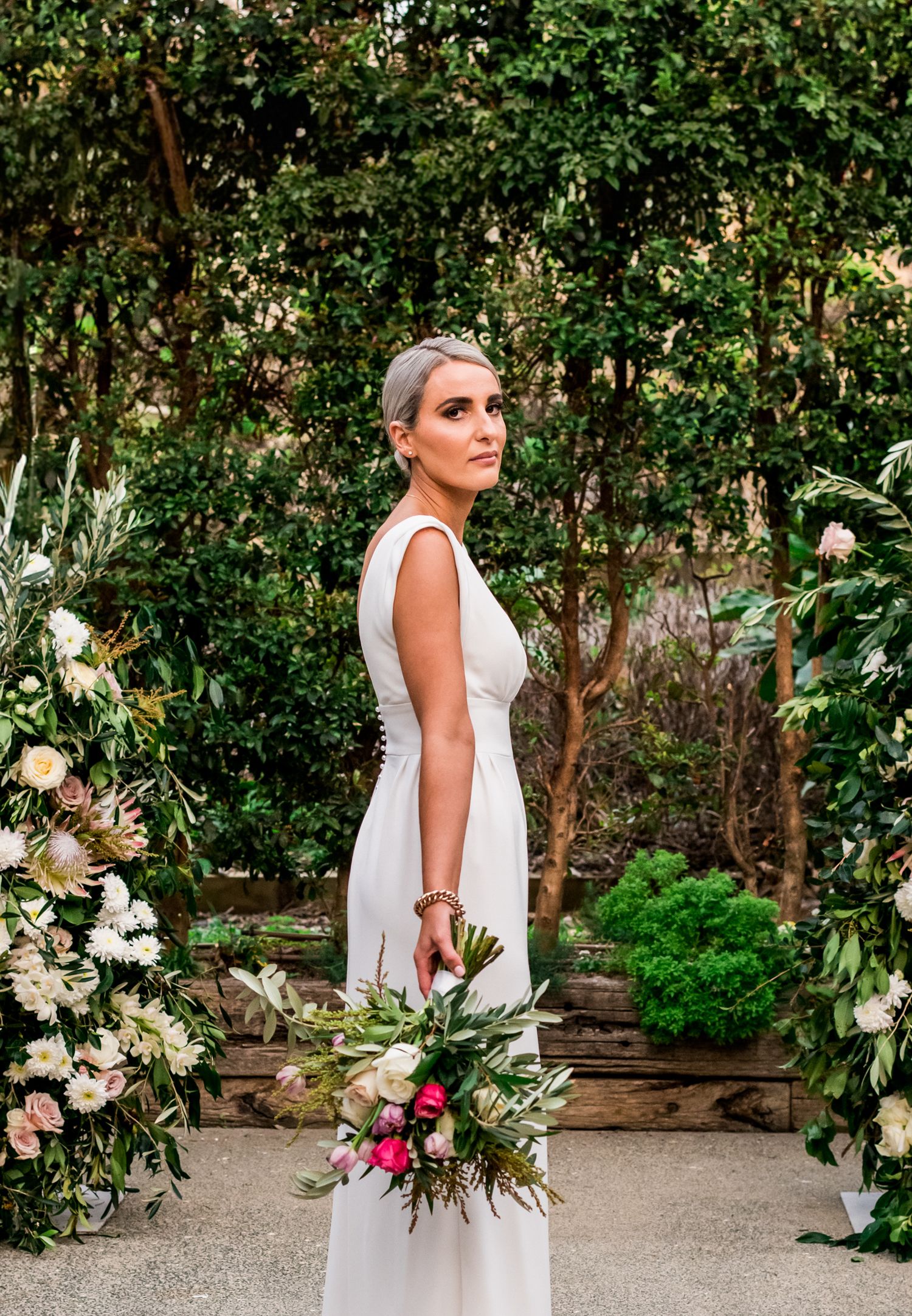 a bride stands in the middle of the Mudbrick wedding venue looking back towards the camera holding her flowers downwards