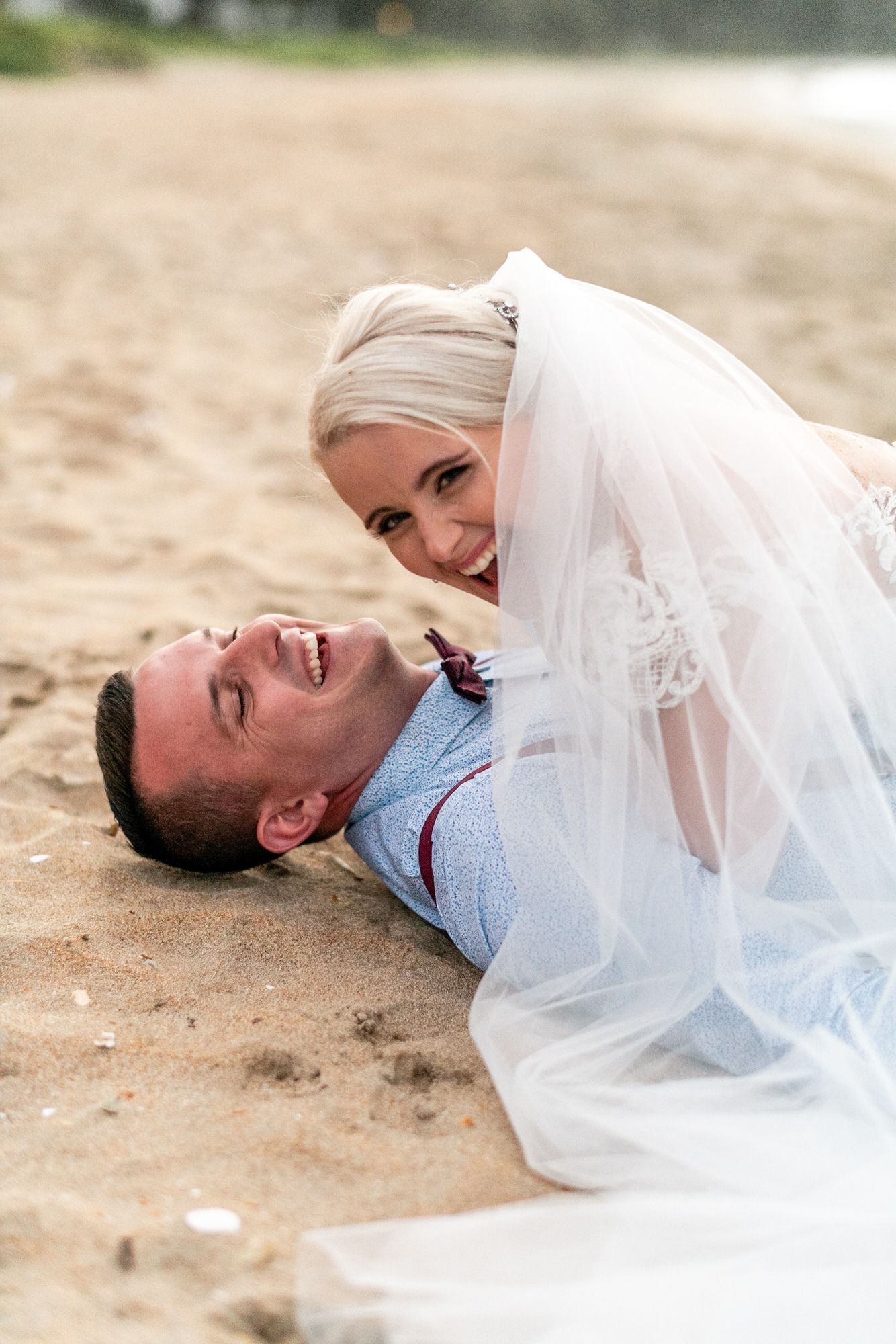 a bride and groom are seen close up lying on a beach, they are really laughing together