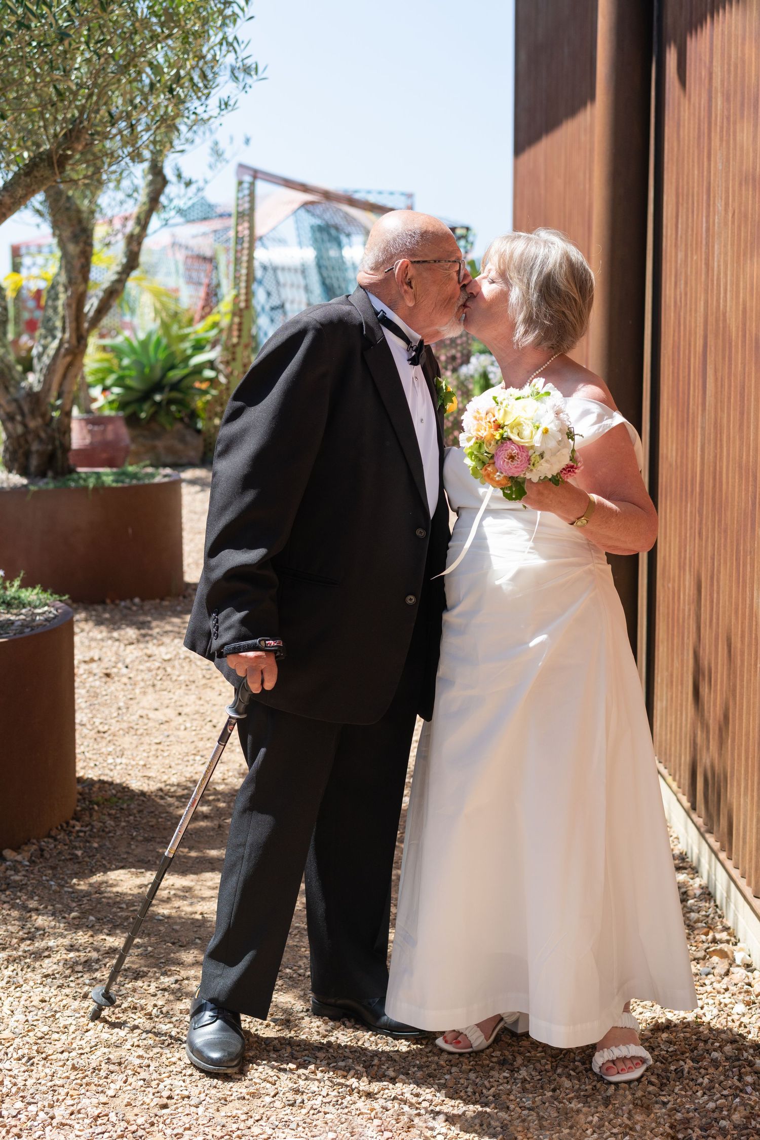 an older couple in wedding attire are having a kiss mid walking at Batch Winery