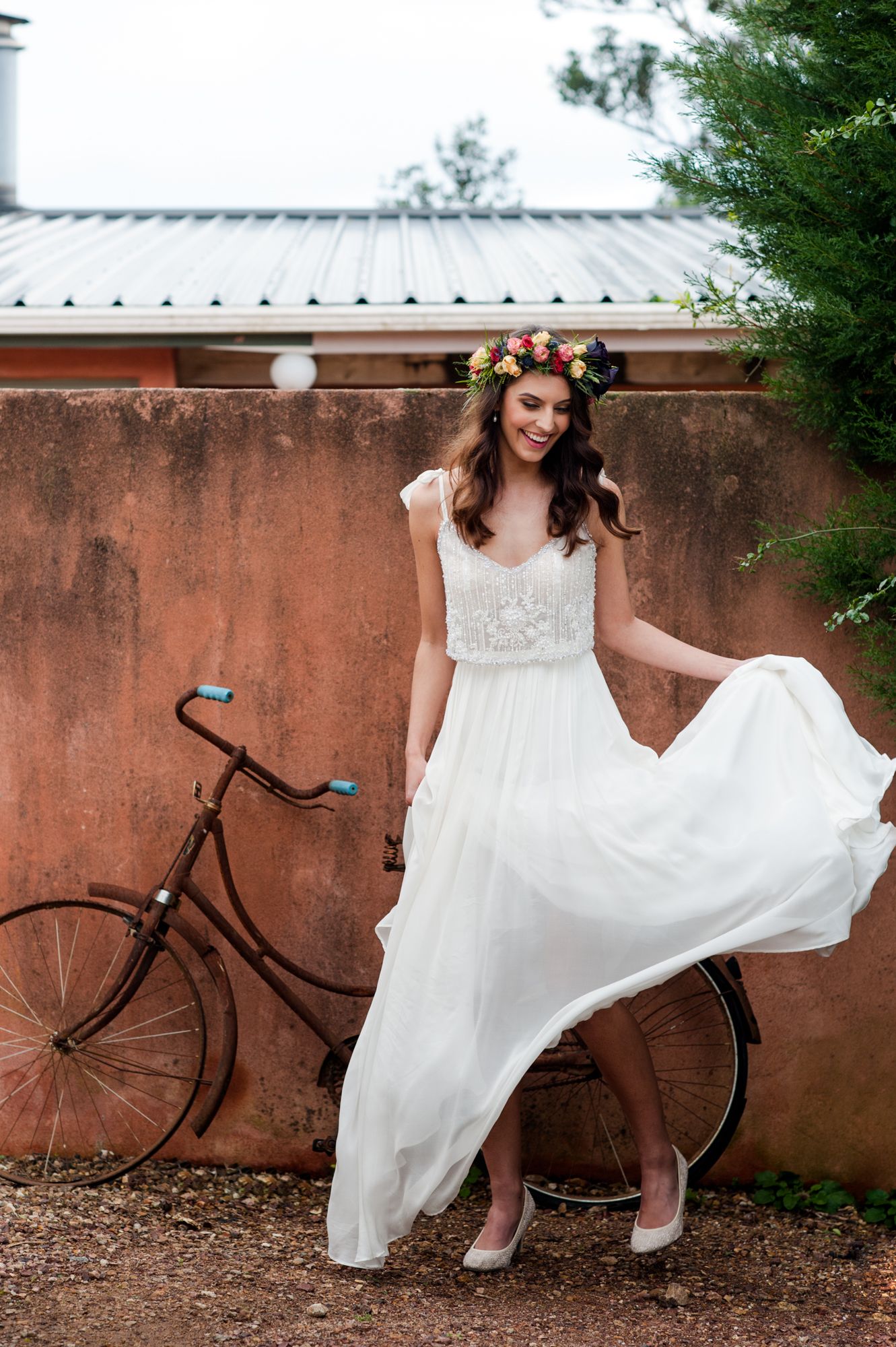 a bride shakes the hem of her dress to create movement, she has a fun smiling face. In the background is an old bicycle at Casita  Miro