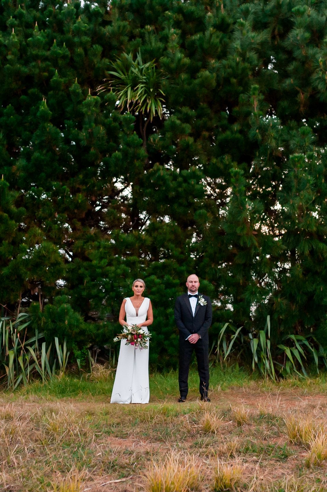 a bride and groom stand side by side looking straight forward towards the camera in a dead pan way creating a fun effect for a portrait