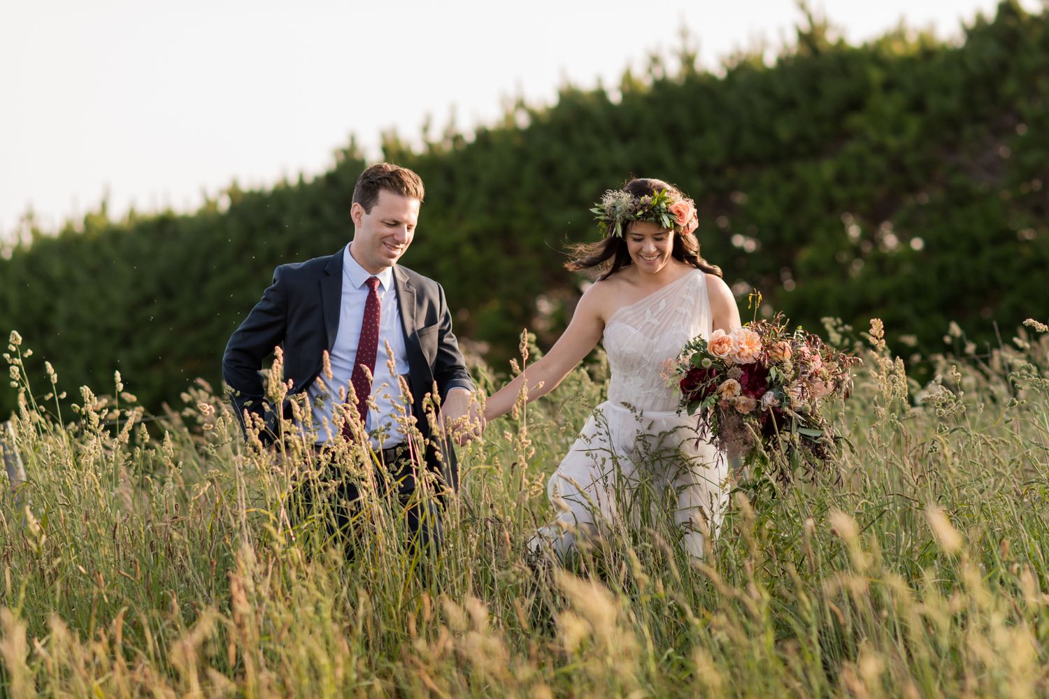 a couple run towards the camera through the long grass of Mudbrick hill, Waiheke