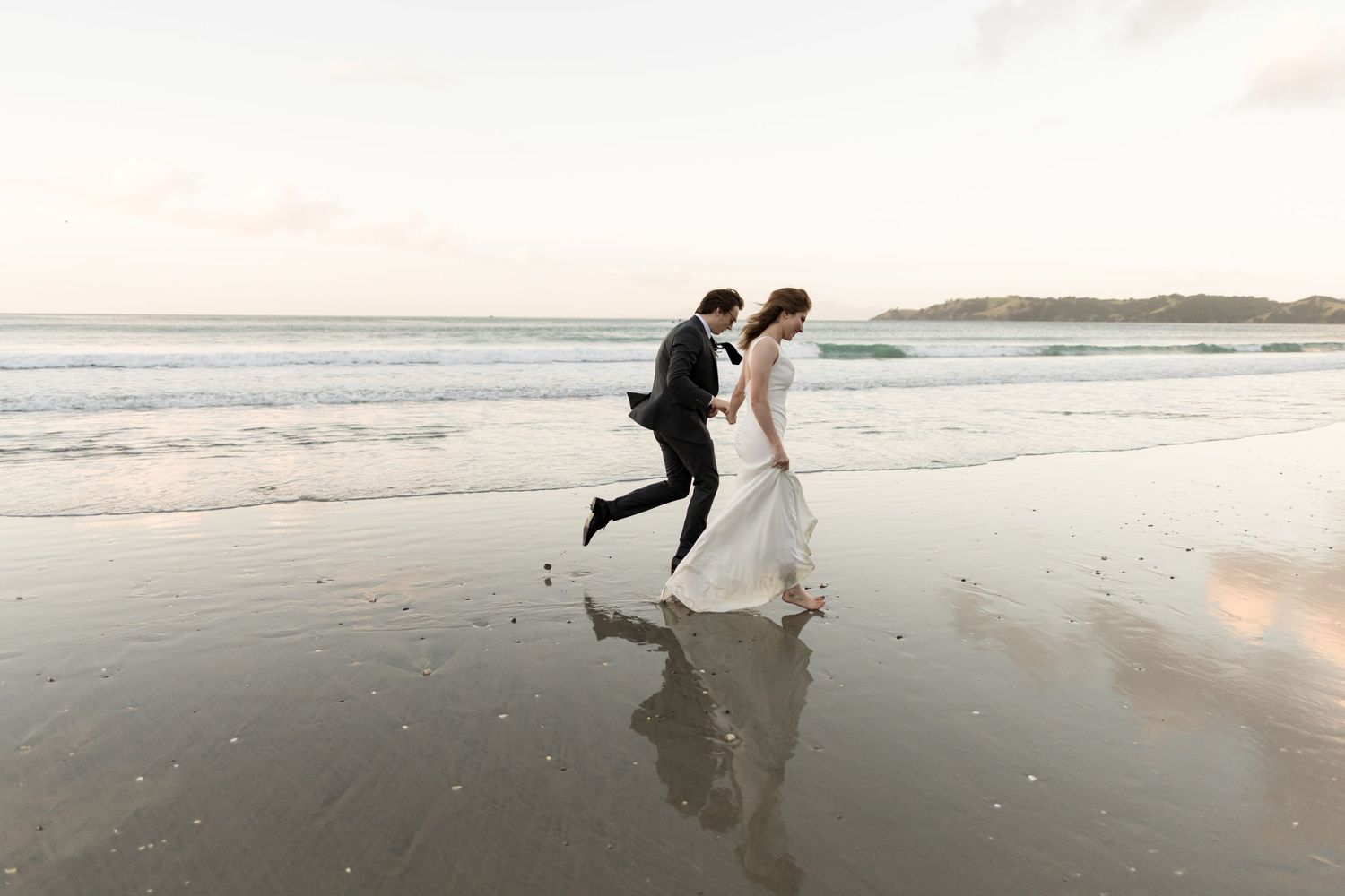 A couple run together with lots of energy holding hands along Onetangi beach, Waiheke Island