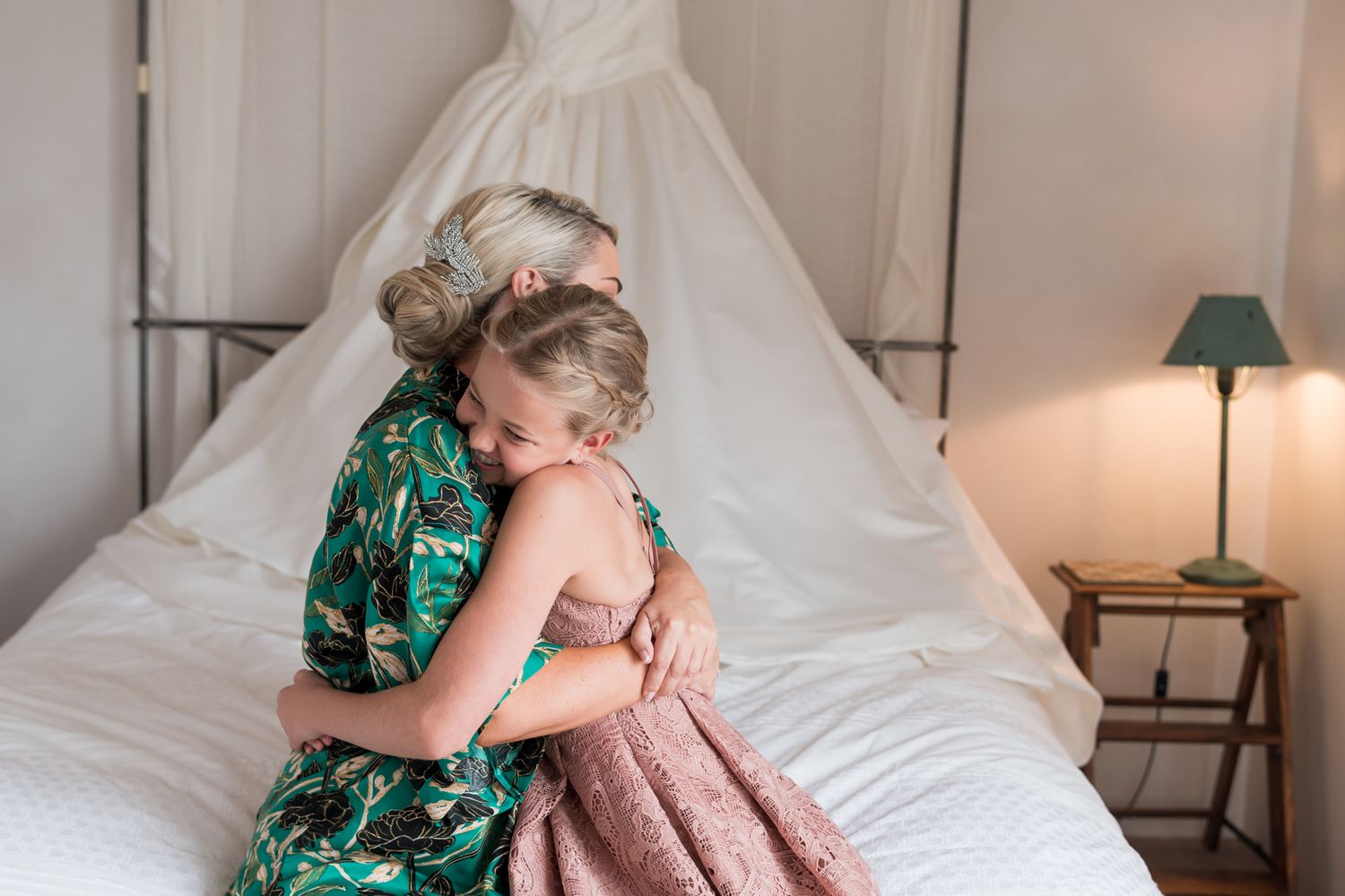 a bride cuddles her daughter on the edge of the bed, she is happy and the cuddle is spontaneous and natural