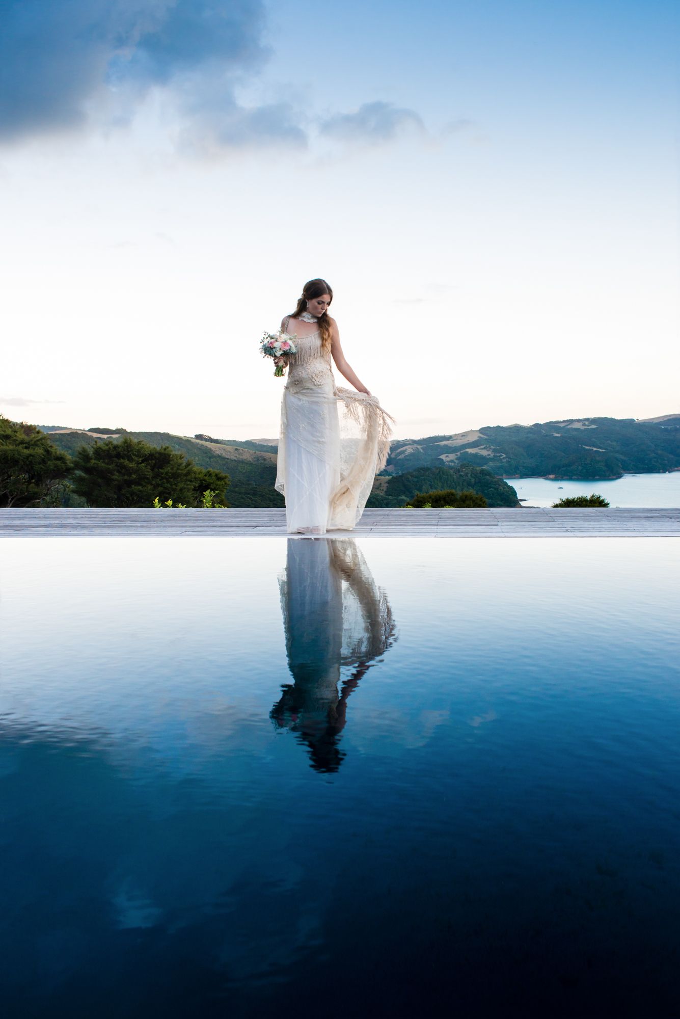 a beautiful image of a bride standing on the edge of a pool with the dark blue sky reflected, it creates a stunning reflection of the bride