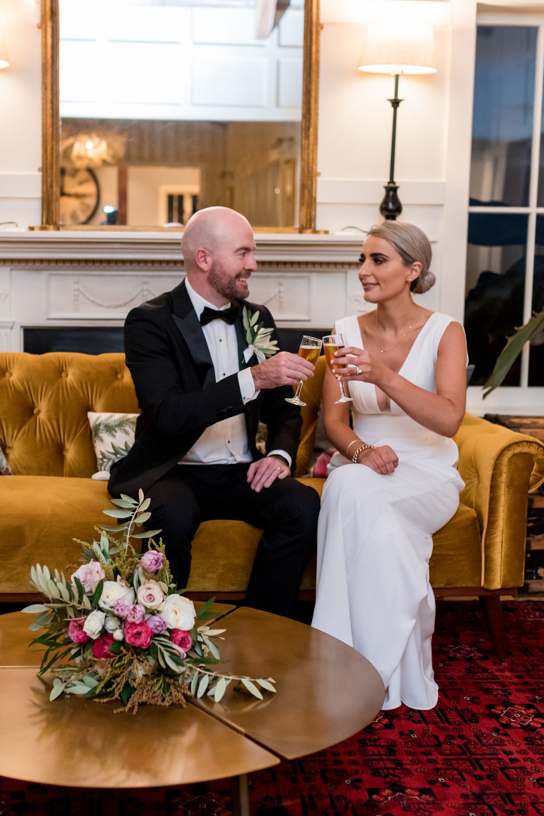 at Mudbrick a bride and groom sit on a velvet gold sofa having a cheers with champagne and smiling