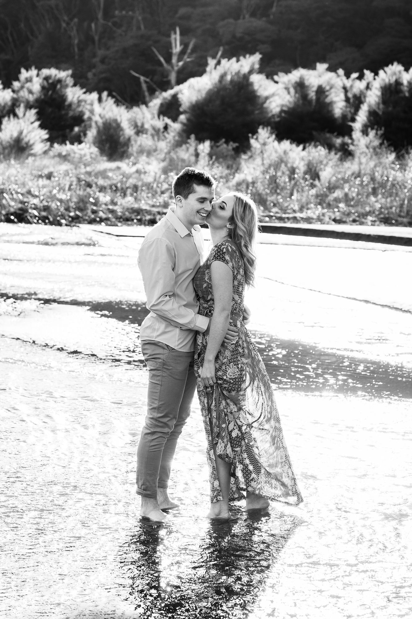 a back lit black and white image of a wedding couple standing in a shallow but wide river with beautiful reflective light all around them