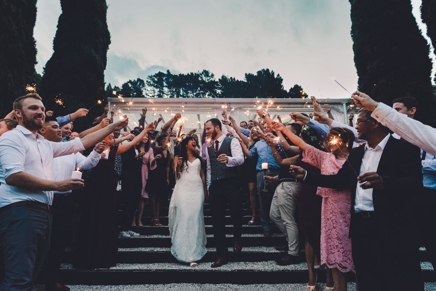 sparklers frame the bride and groom from their guests as they walk down the stairs towards the camera