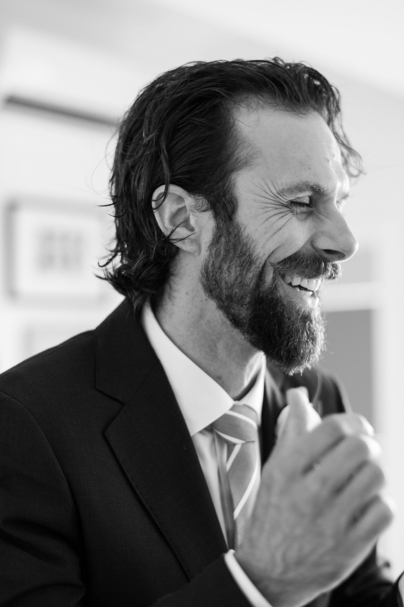 a black and white image of a groom naturally laughing off to the side of the camera