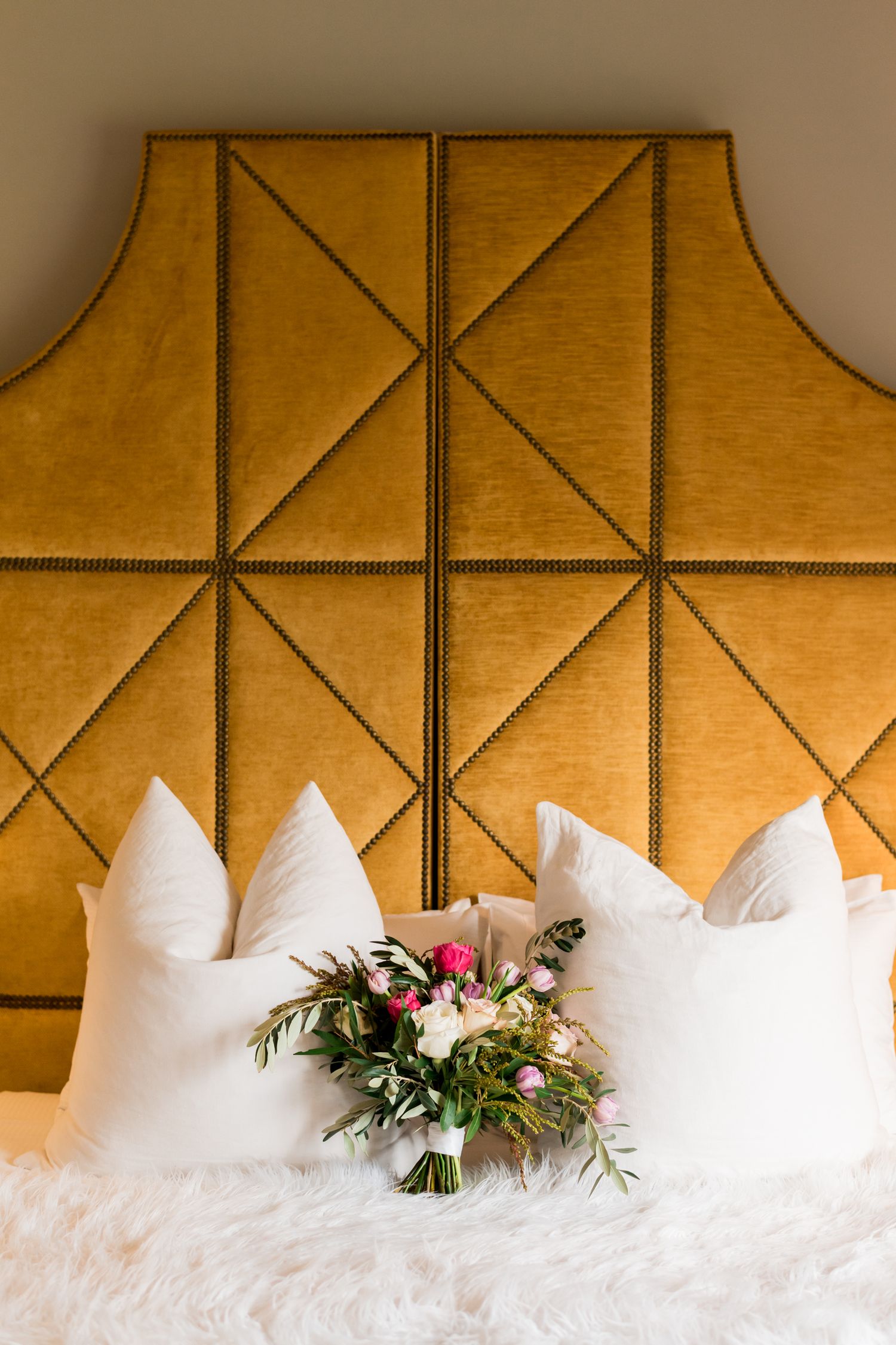 a still life of a bouquet of flowers snuggled in the pillows with the golden velvet headboard behind adding elegance