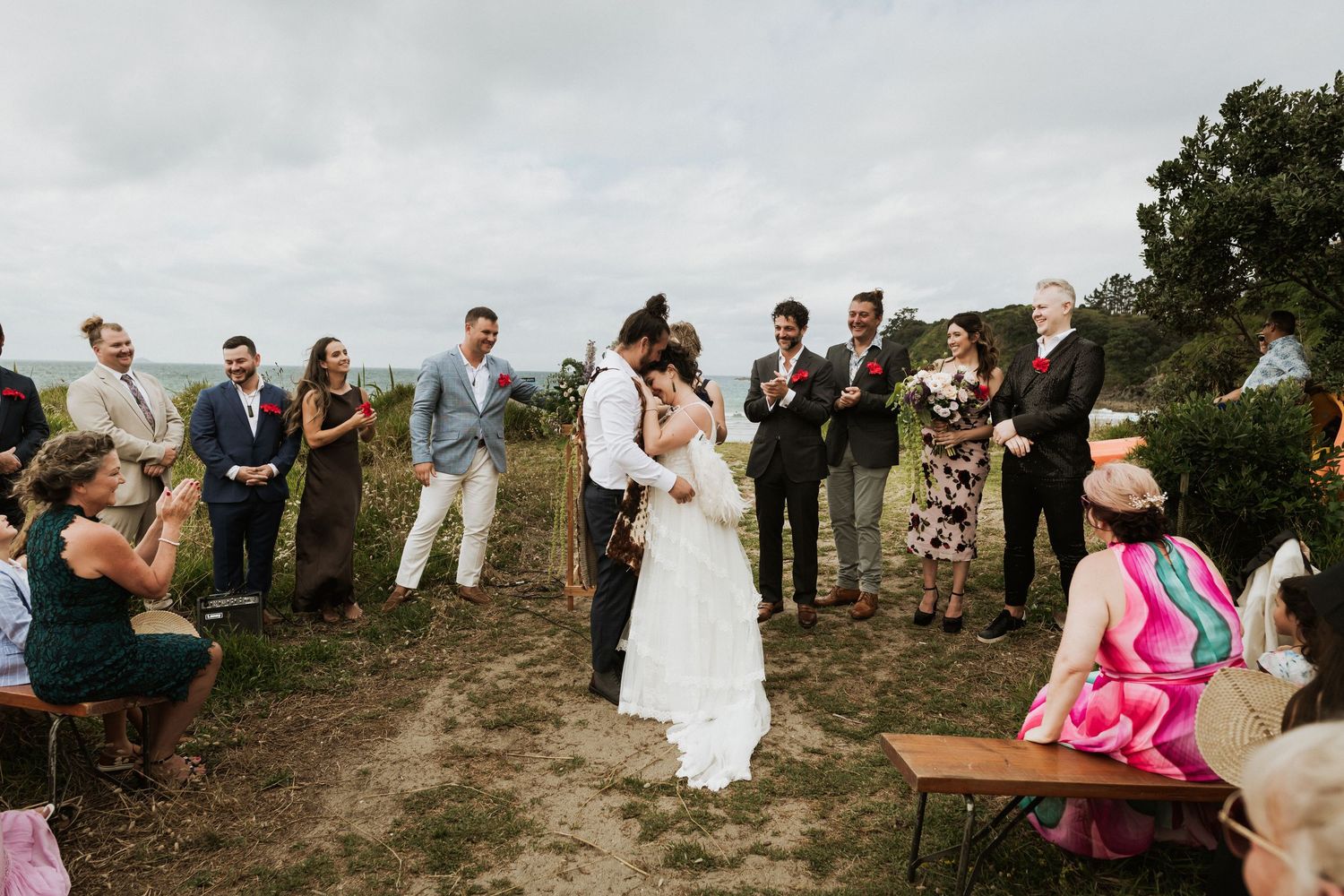 A couple embrace on their wedding day ceremony with their friends and family around them