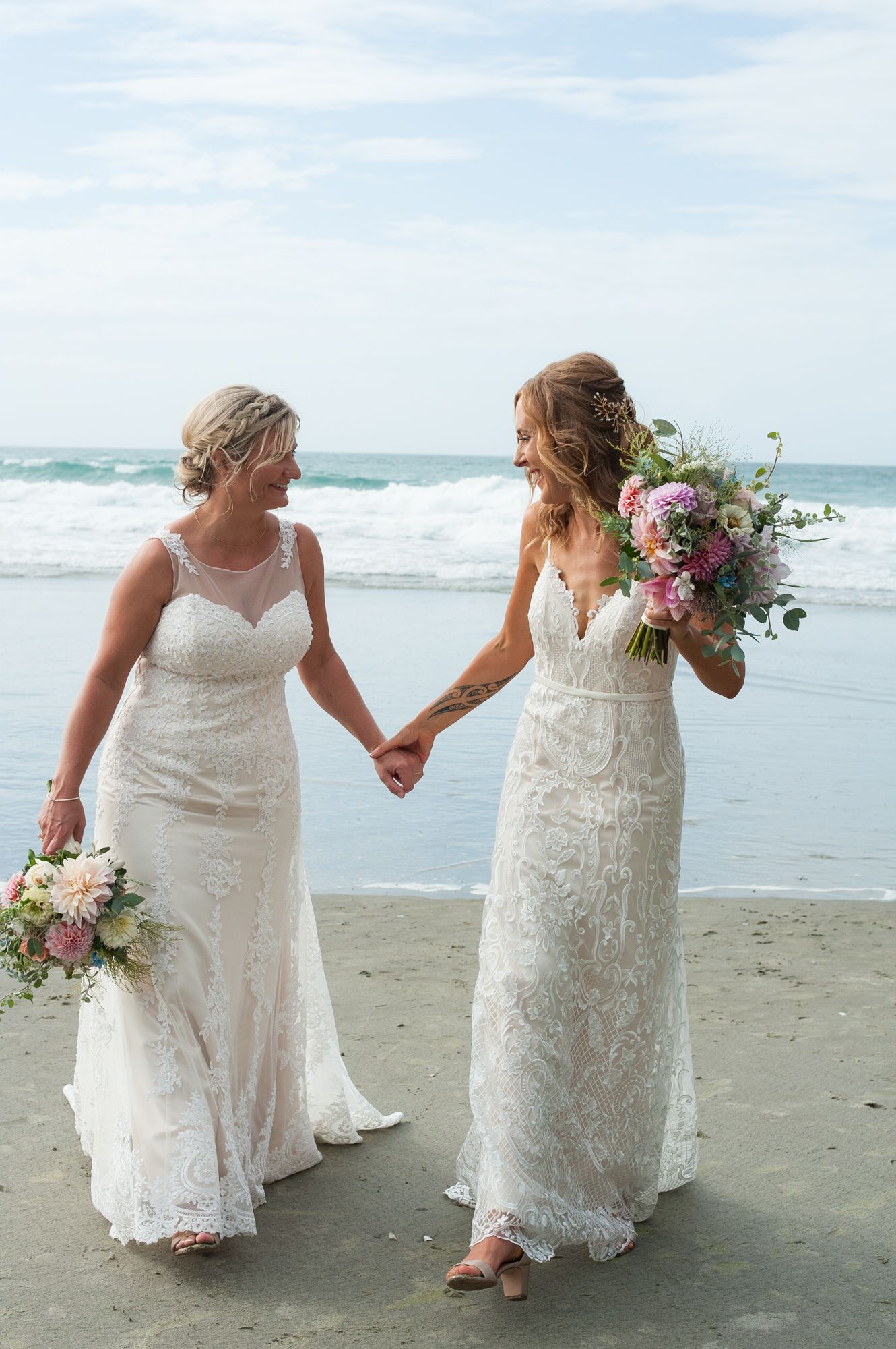 Double brides on their wedding day walking towards the camera happy smiling and holding hands on Onetangi beach