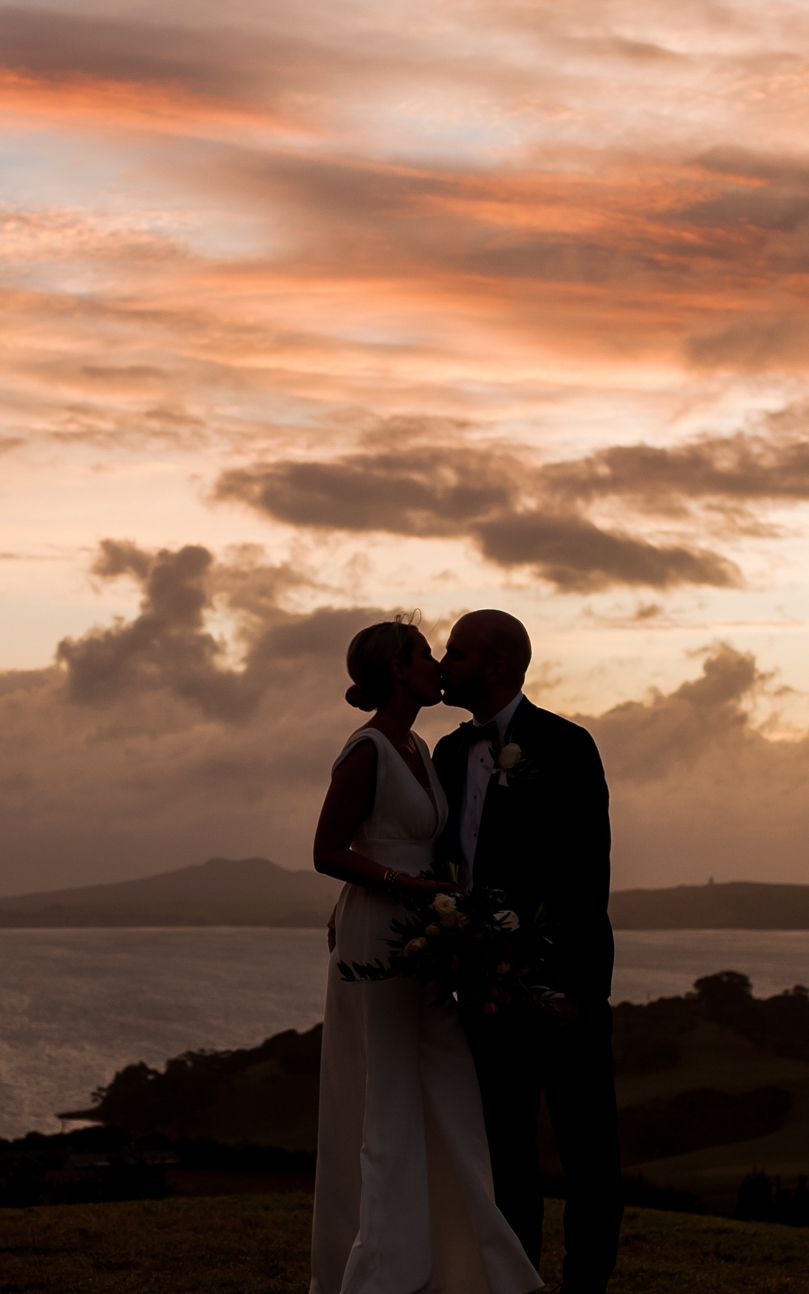 a silhouette of a bride and groom embracing with a dramatic orange and apricot sky behind
