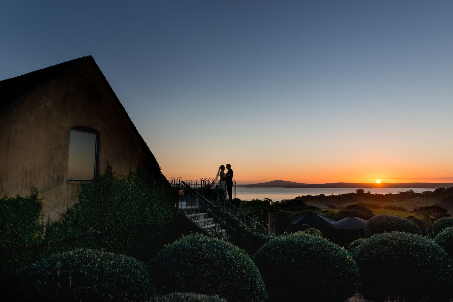 a magnificent photo of a stunning dark blue and vivid orange sunset with the Mudbrick venue, the bride and groom standing on the balcony