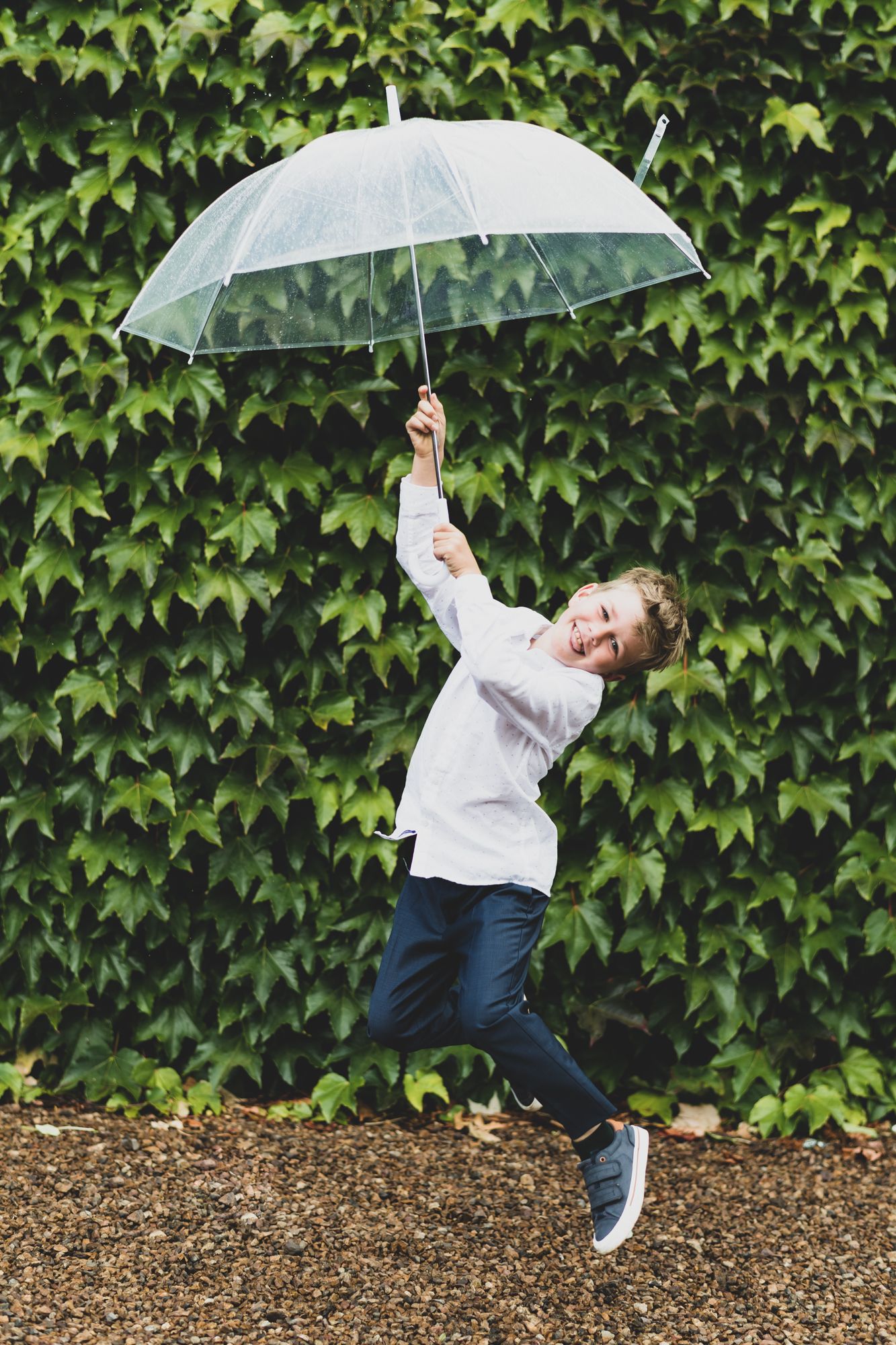 a young page boy jumps in front of a wall of ivy having fun with an umbrella at Poderi Crisci