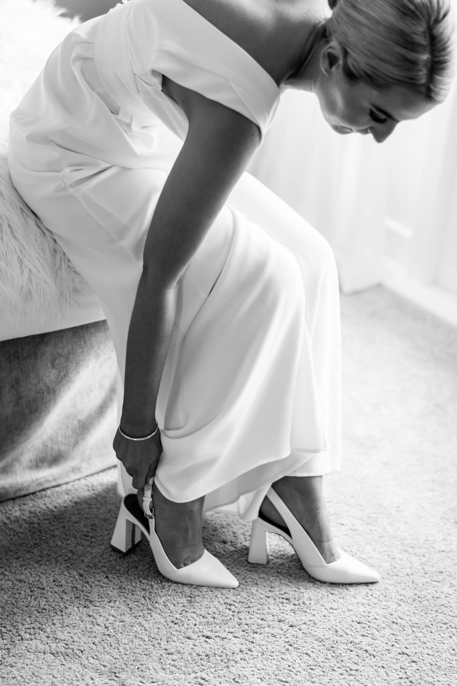 a black and white image of a bride leaning down and pulling on the back of her show