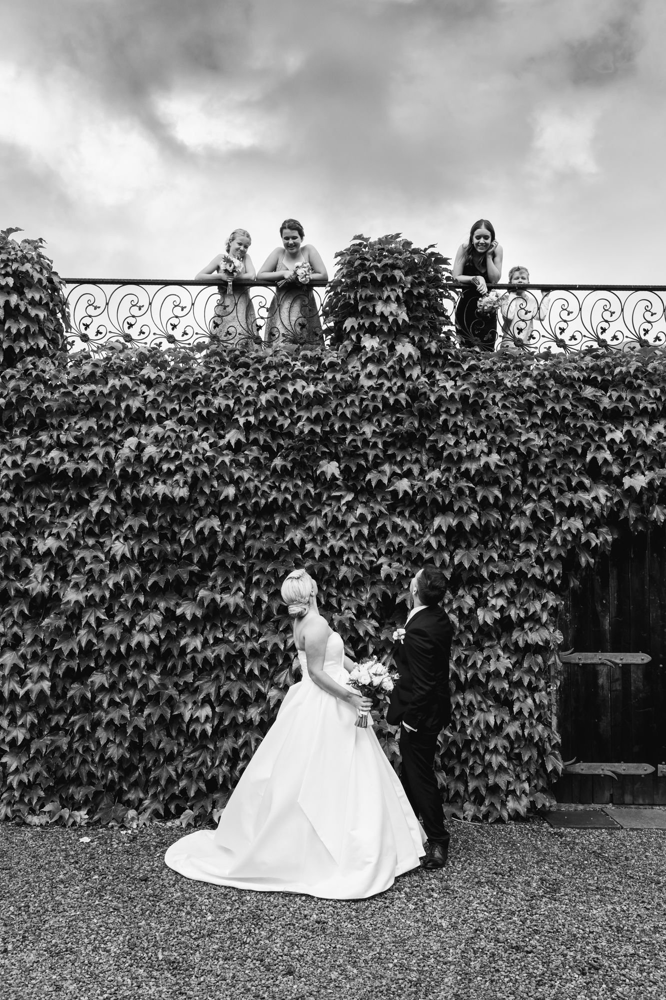 a black and white image of a bride and groom looking up at their young wedding party who are looking down at them from the railings