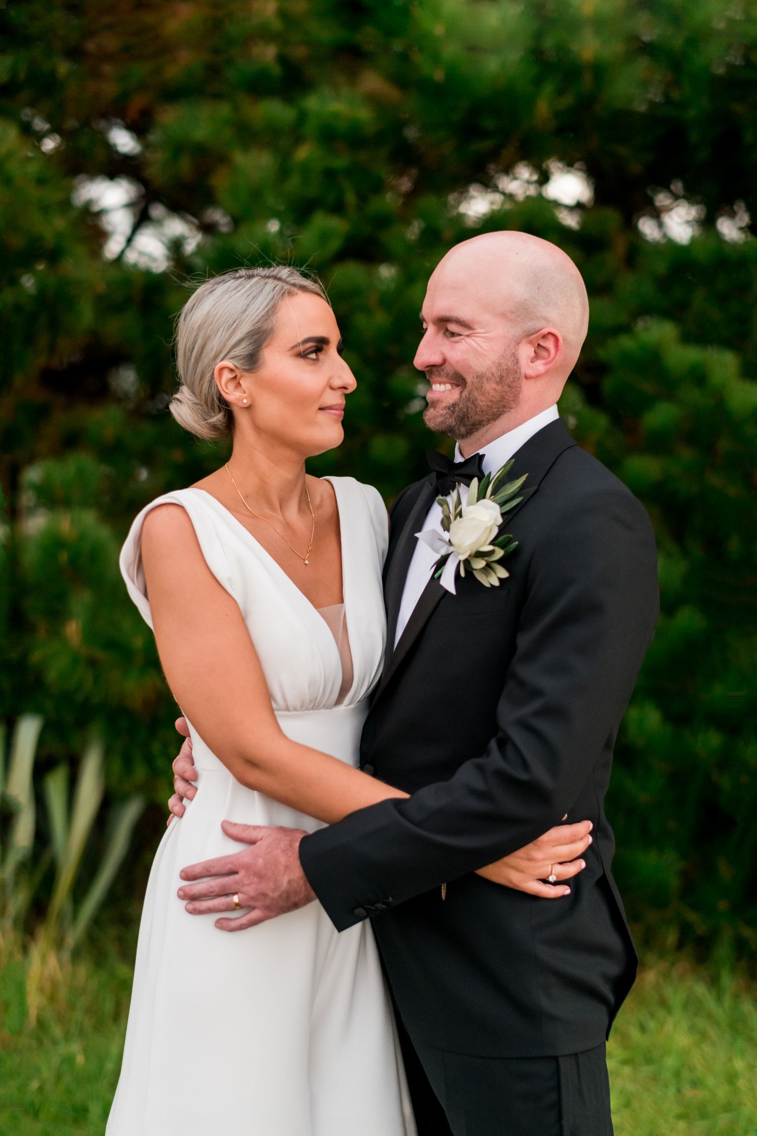 a bride and groom look at each other whilst wrapping their arms around each other holding together in closeness