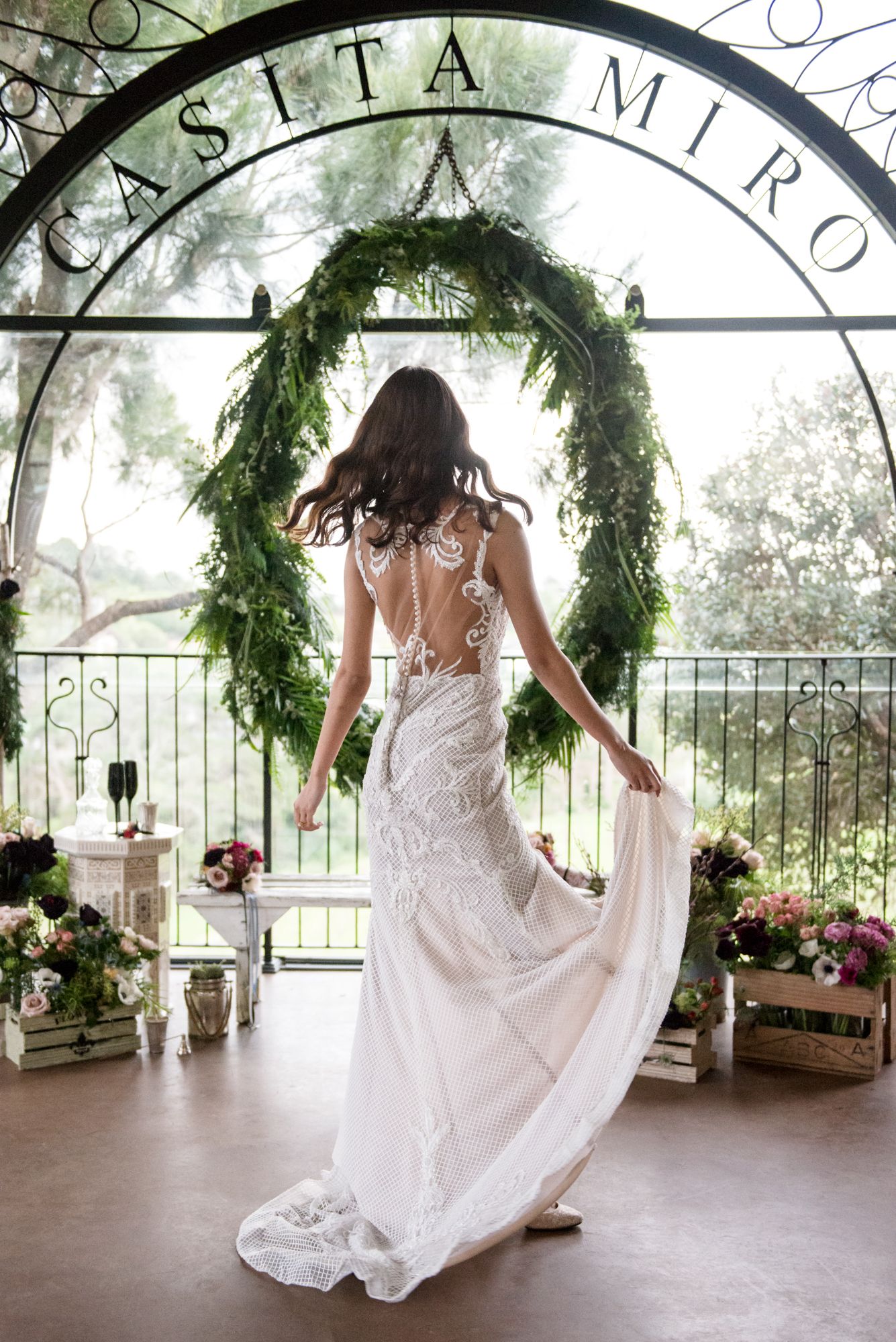 a bride spins holding her dress aside in front of a big arched window and beautiful flowers at Casita Miro