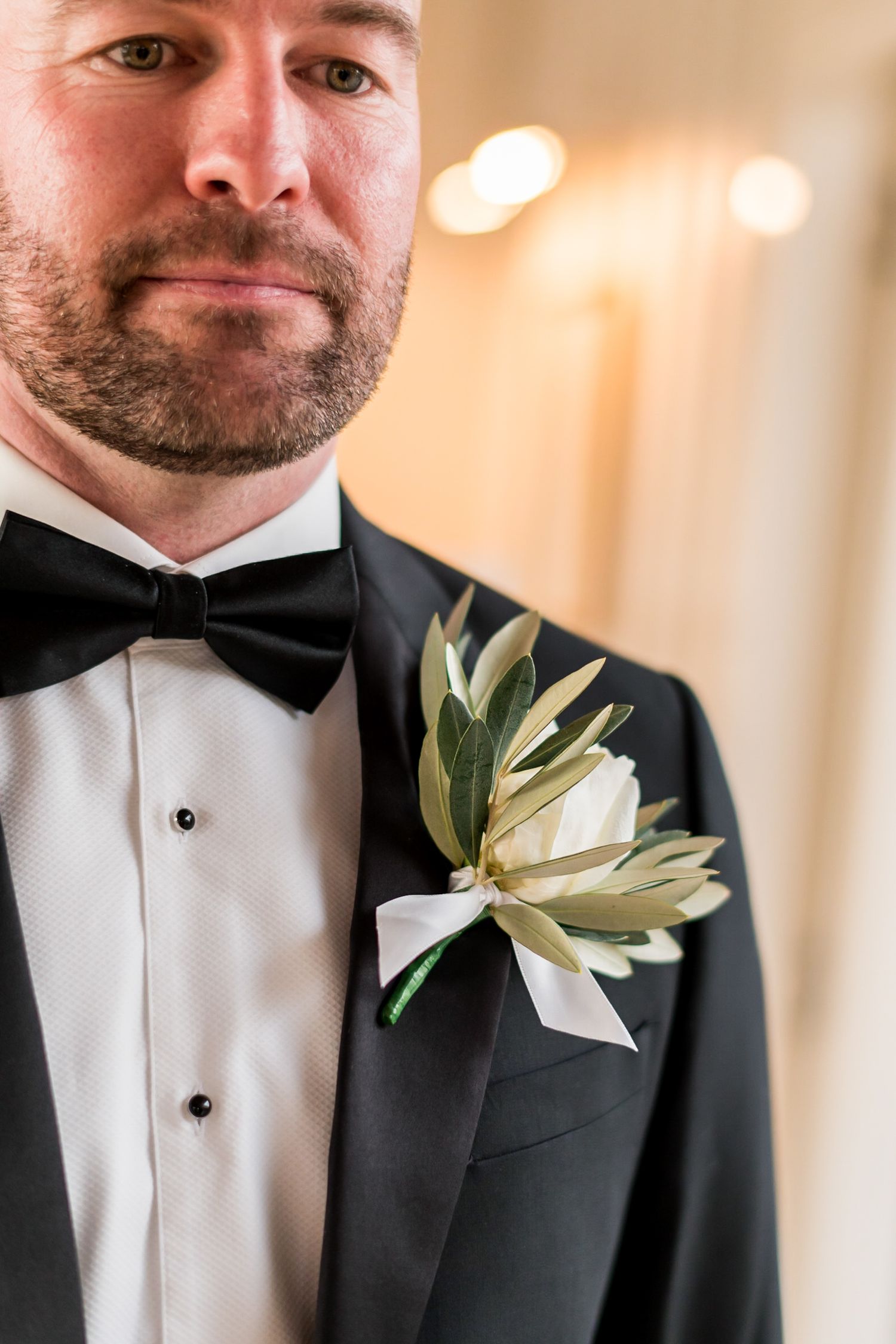 a close up of a groom and his attire showing off his button hole and bow tie
