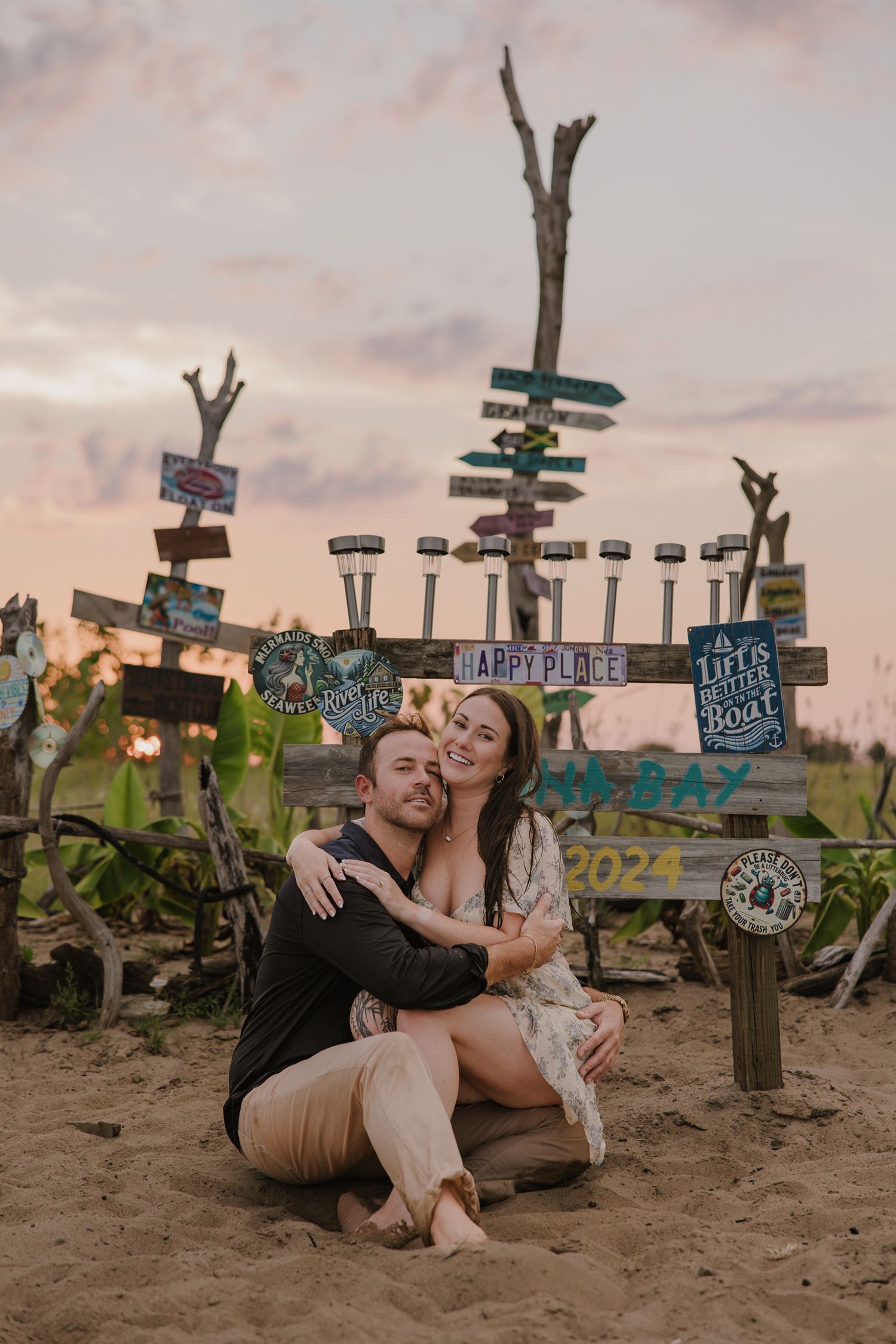 Romantic couple poses by colorful directional signs on a beach at sunset.