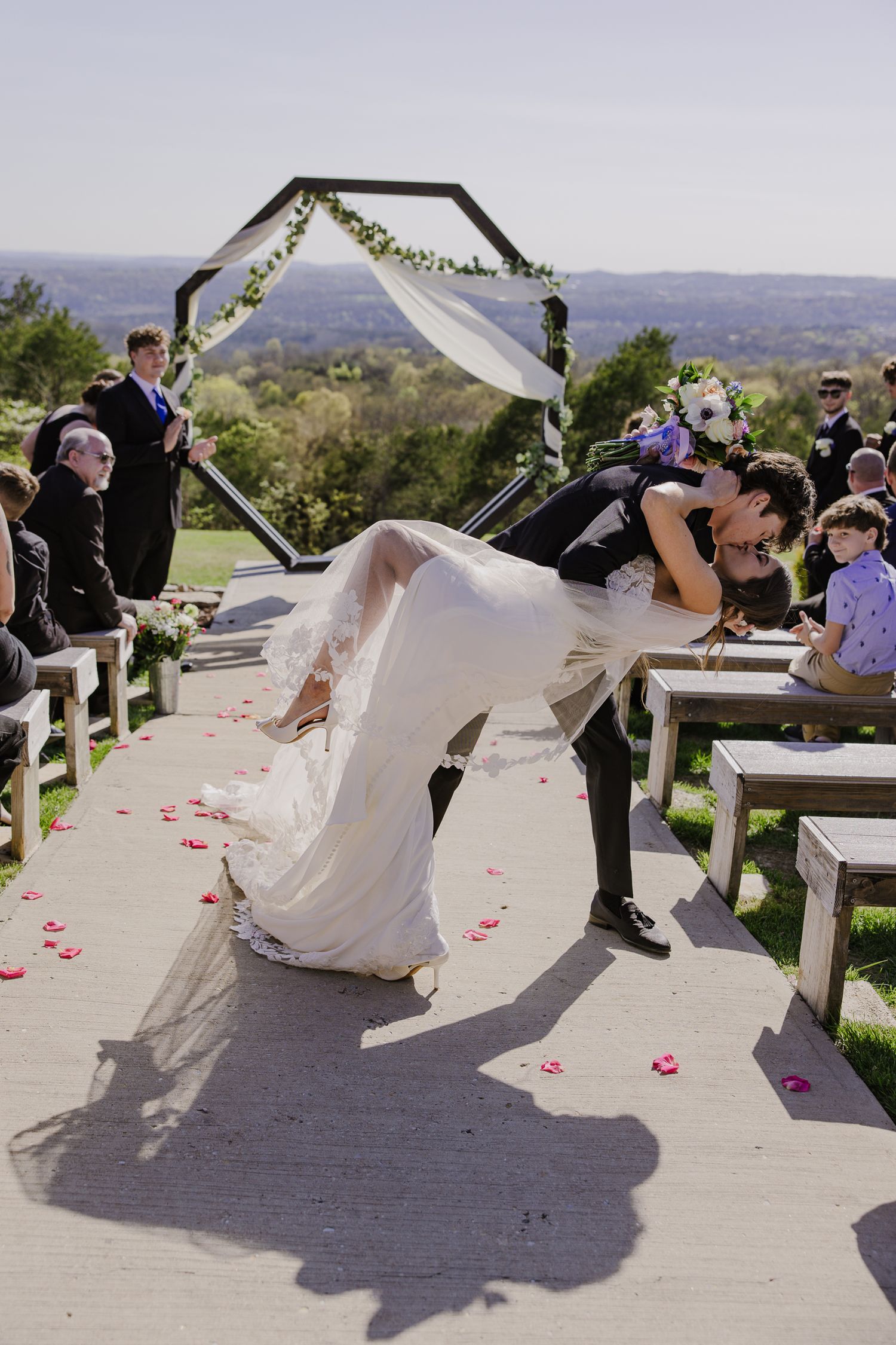 Wedding couple performs dramatic dip pose on outdoor deck with mountain views.