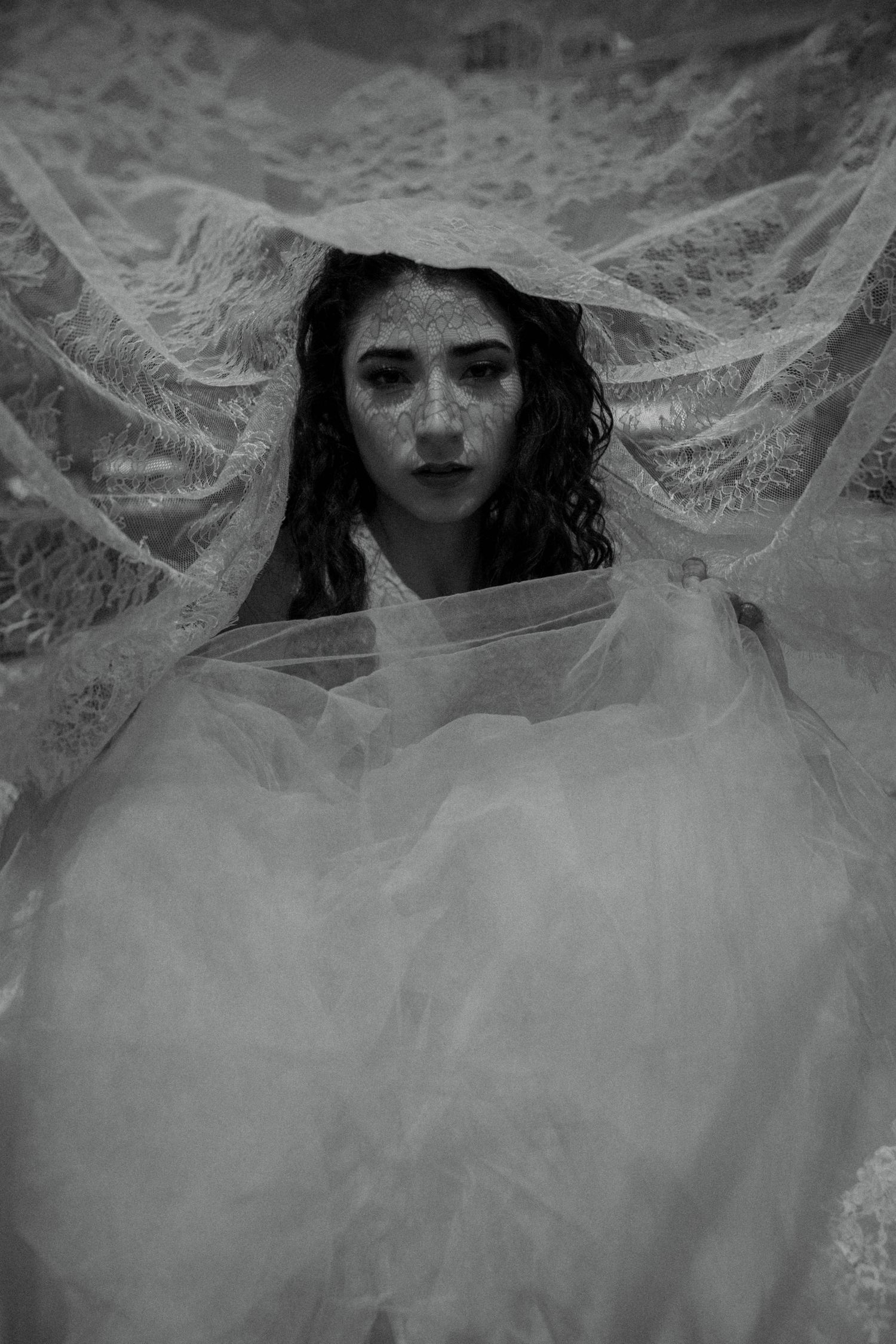 Black and white portrait of a bride draped in sheer lace veil wearing a white tulle wedding gown.