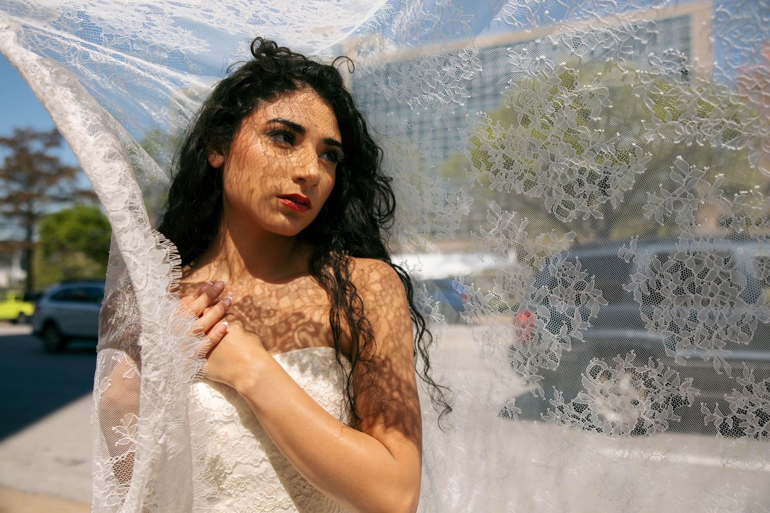 Close-up of bride in lace veil with bold red lips and floral henna on skin.