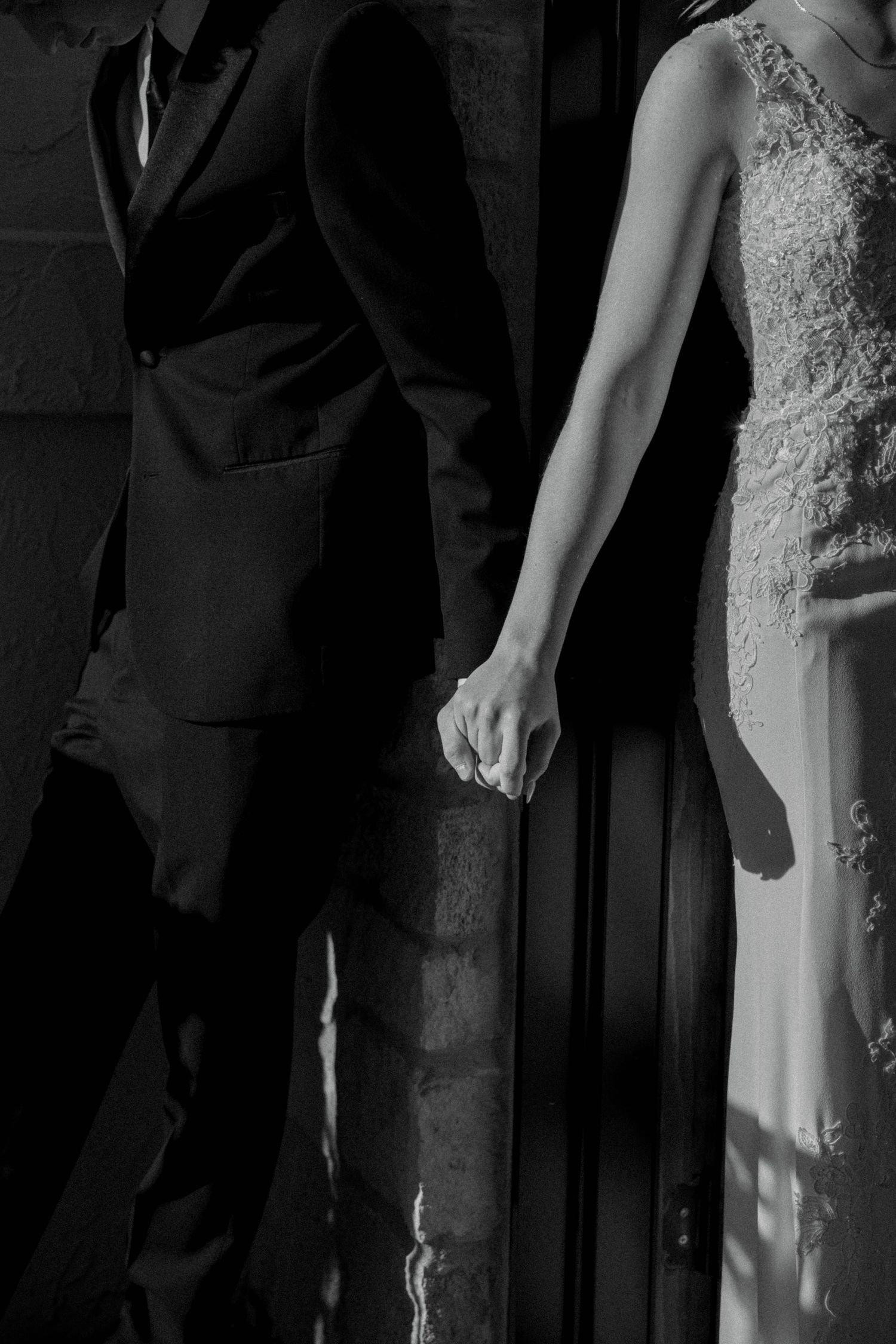 Black and white photo of a bride and groom holding hands in wedding attire.