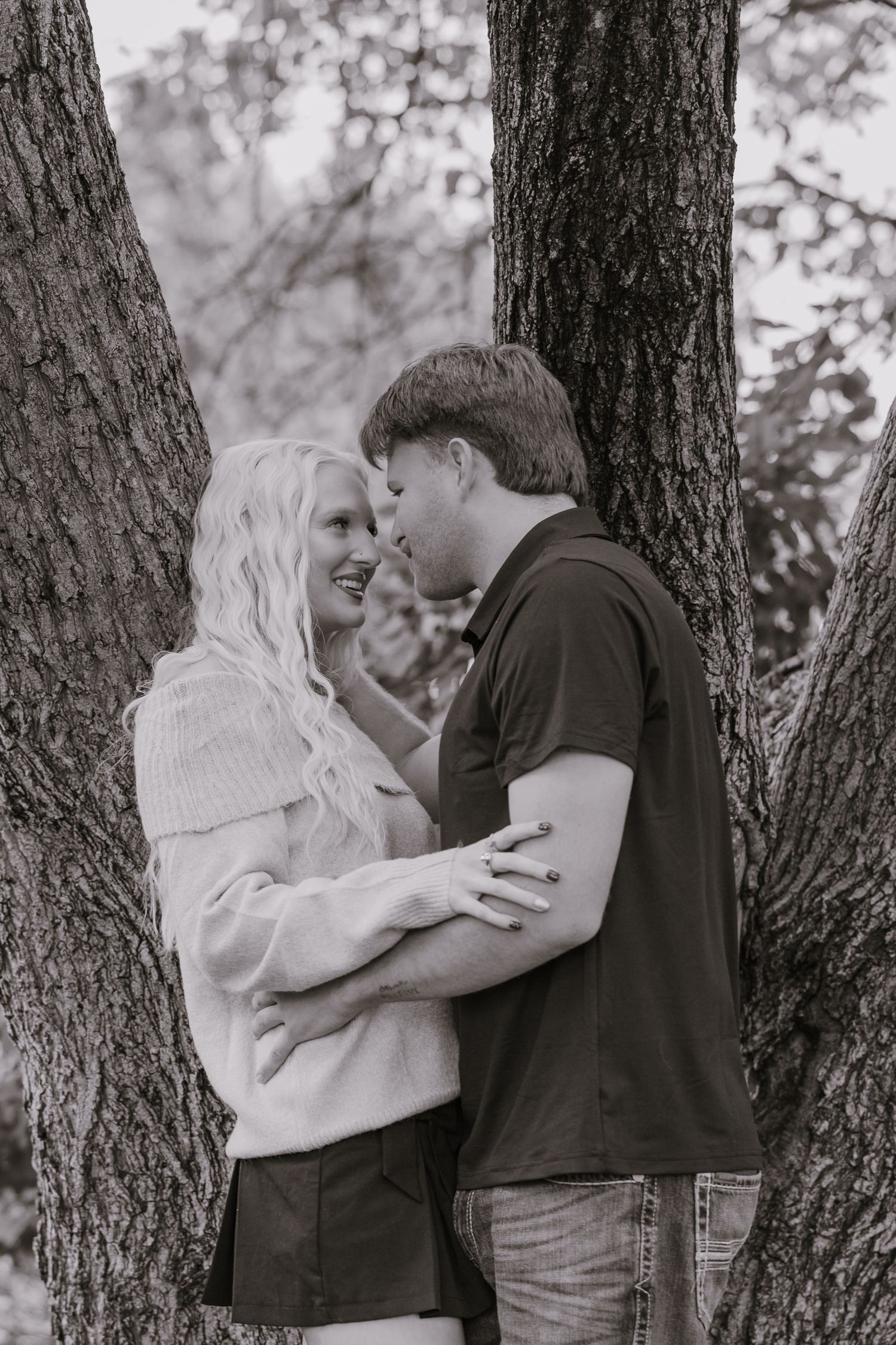 Romantic couple sharing an intimate moment between trees in a black and white outdoor portrait.
