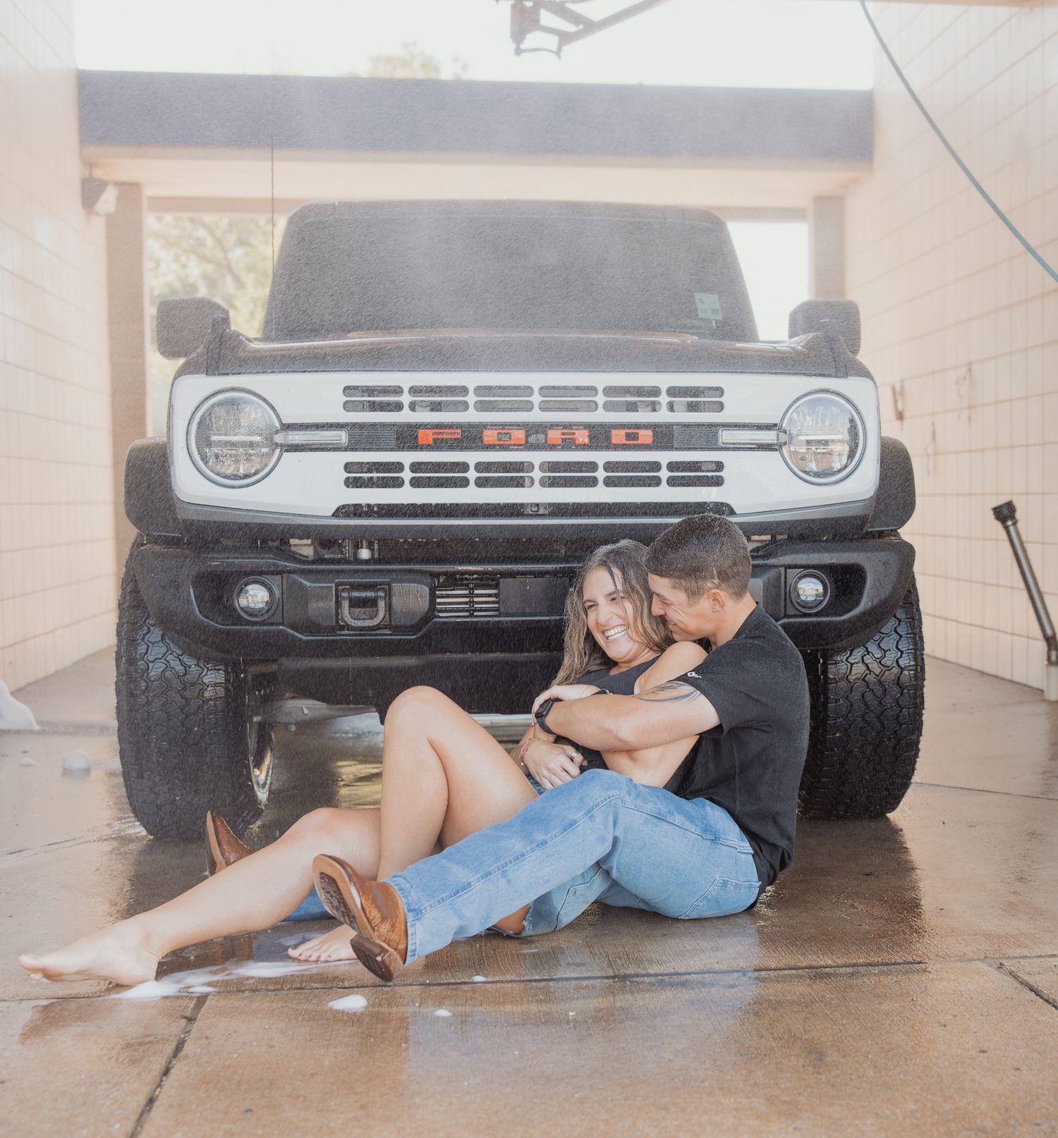 Couple laying on ground in front of black truck in romantic photoshoot sequence.