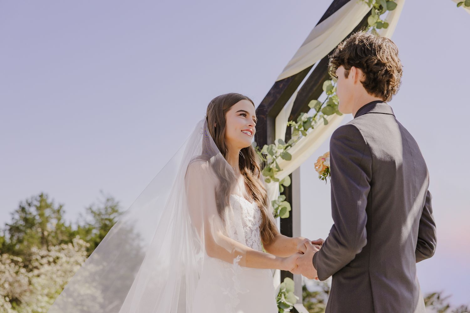 Couple shares intimate moment during wedding ceremony under floral arch.