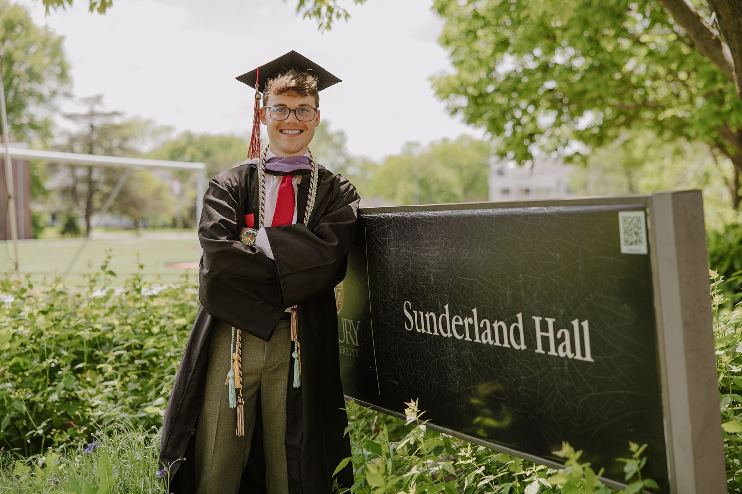 Graduate poses near Sunderland Hall signage during commencement photo session.
