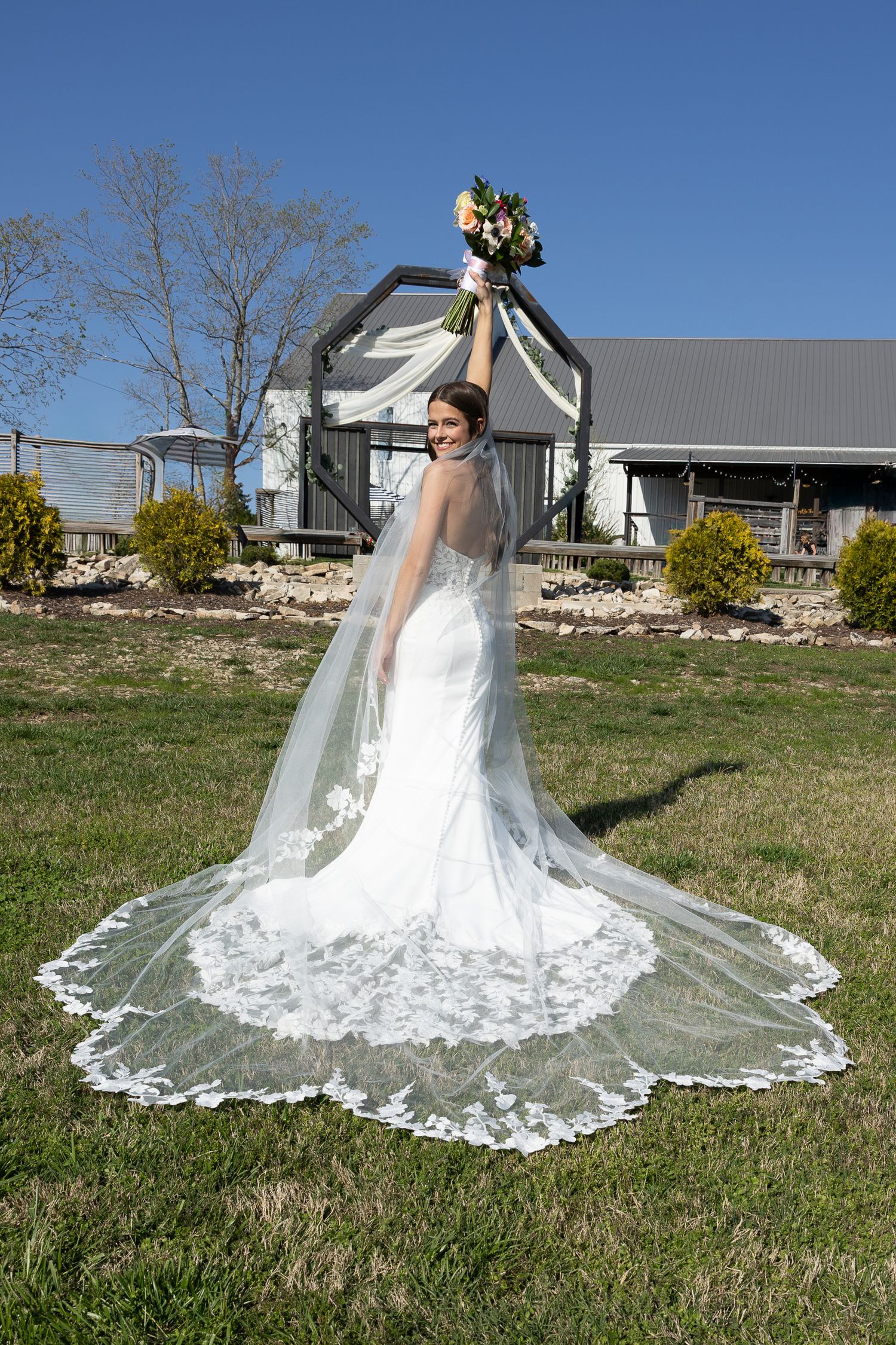 Stunning lace wedding dress with cathedral veil displayed outdoors against blue sky.