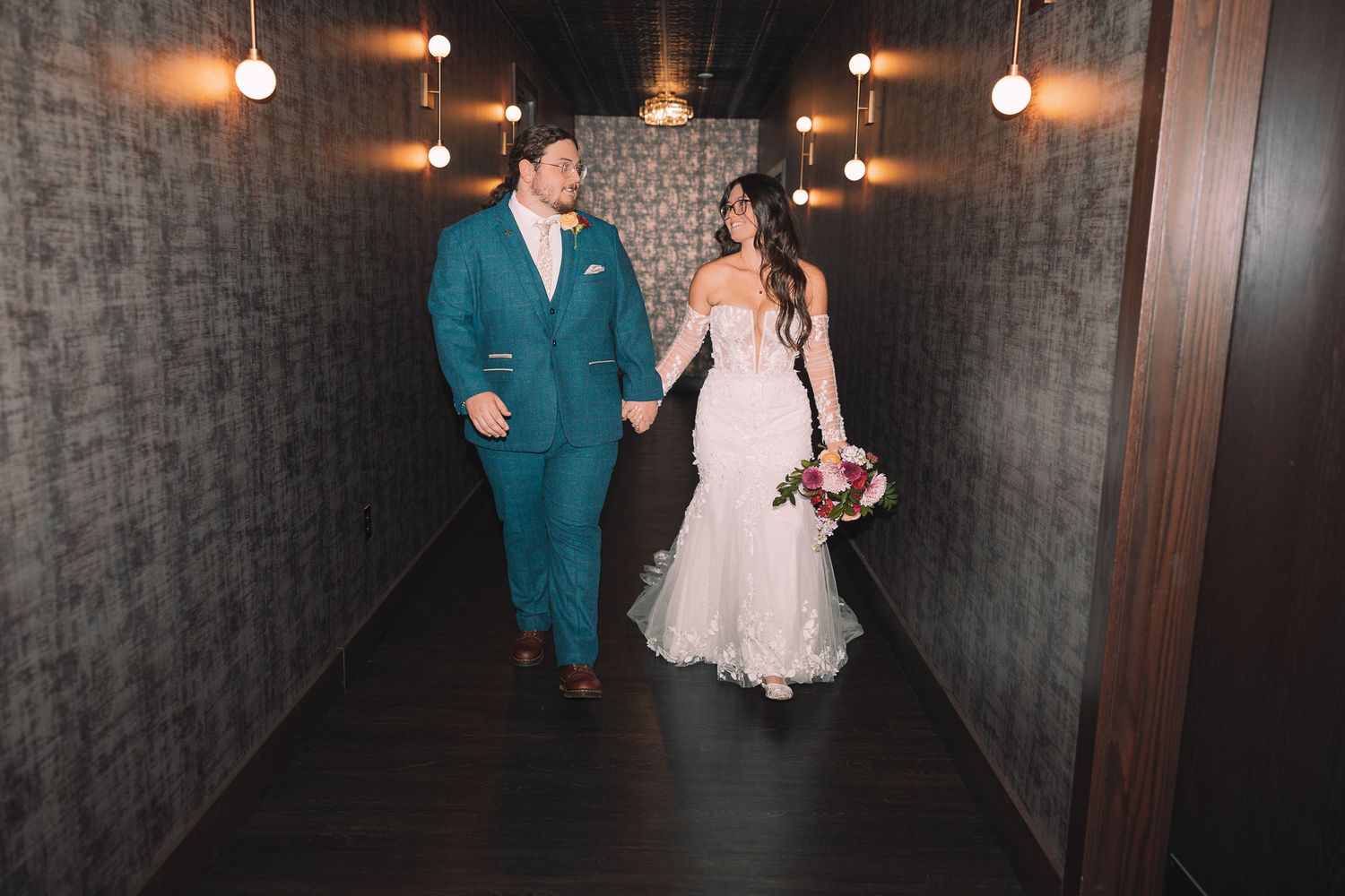 Wedding couple walking through dimly lit hallway with vintage pendant lighting.