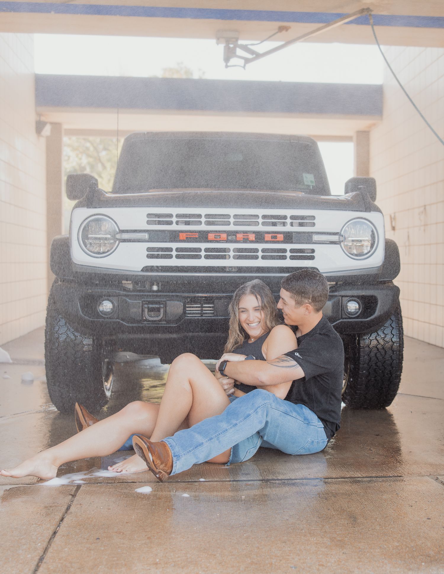 Couple lying beneath a vintage truck in a creative automotive-themed photoshoot series.
