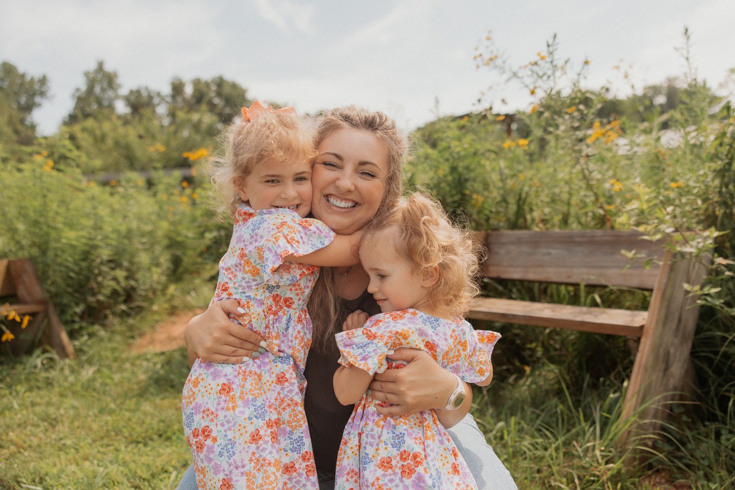 Two people share joyful moments together in a sunny outdoor setting surrounded by greenery.
